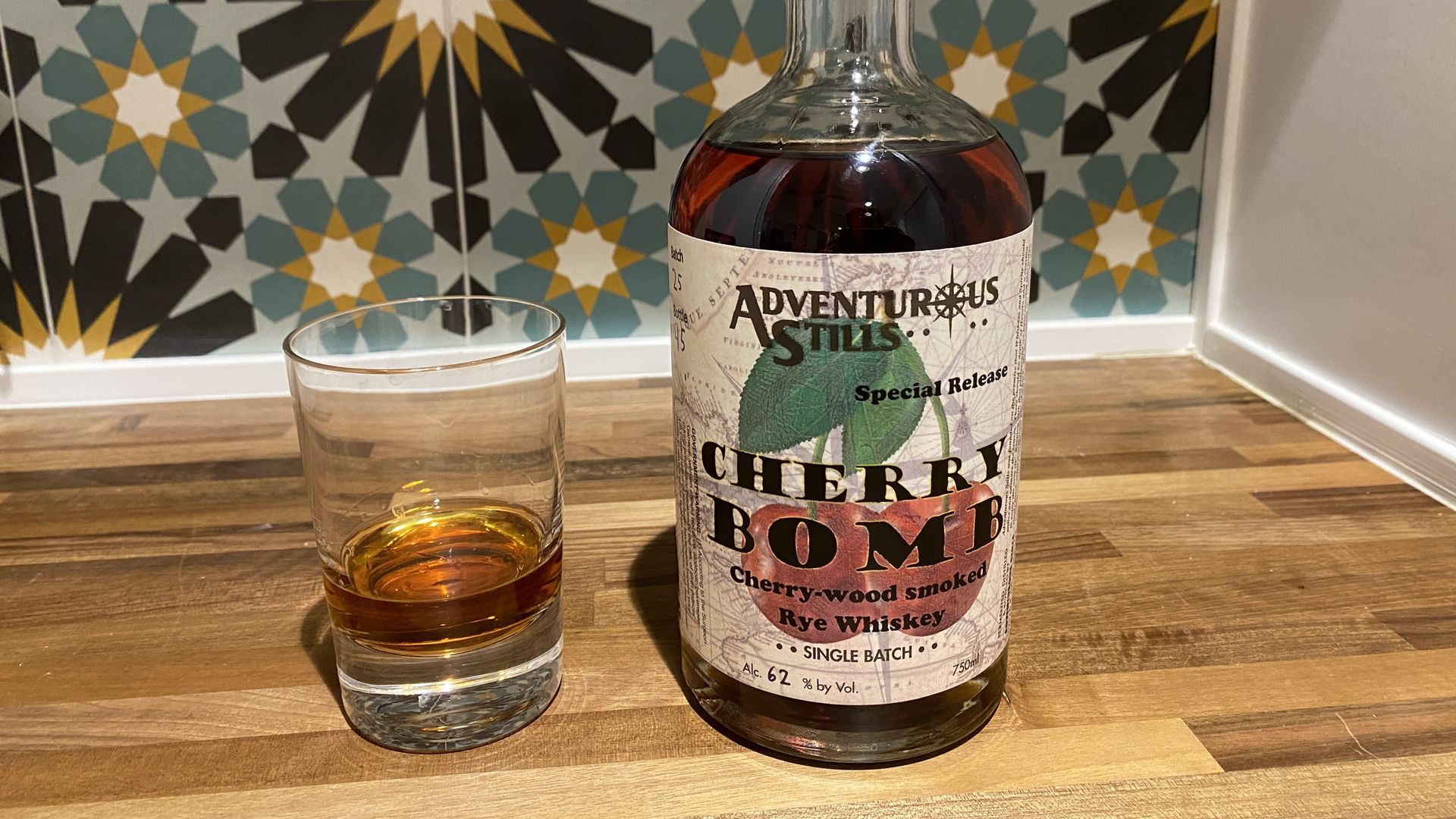 A glass of whiskey next to a bottle labeled Cherry Bomb with a drawing of two cherries