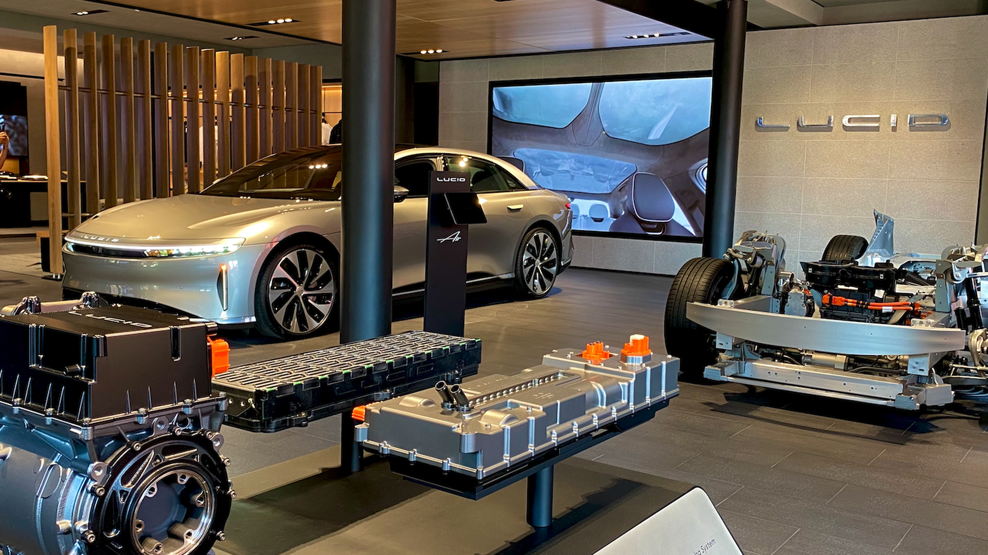 Image of a showroom with a Lucid vehicle in the background and parts of the car displayed on the showroom floor in the foreground
