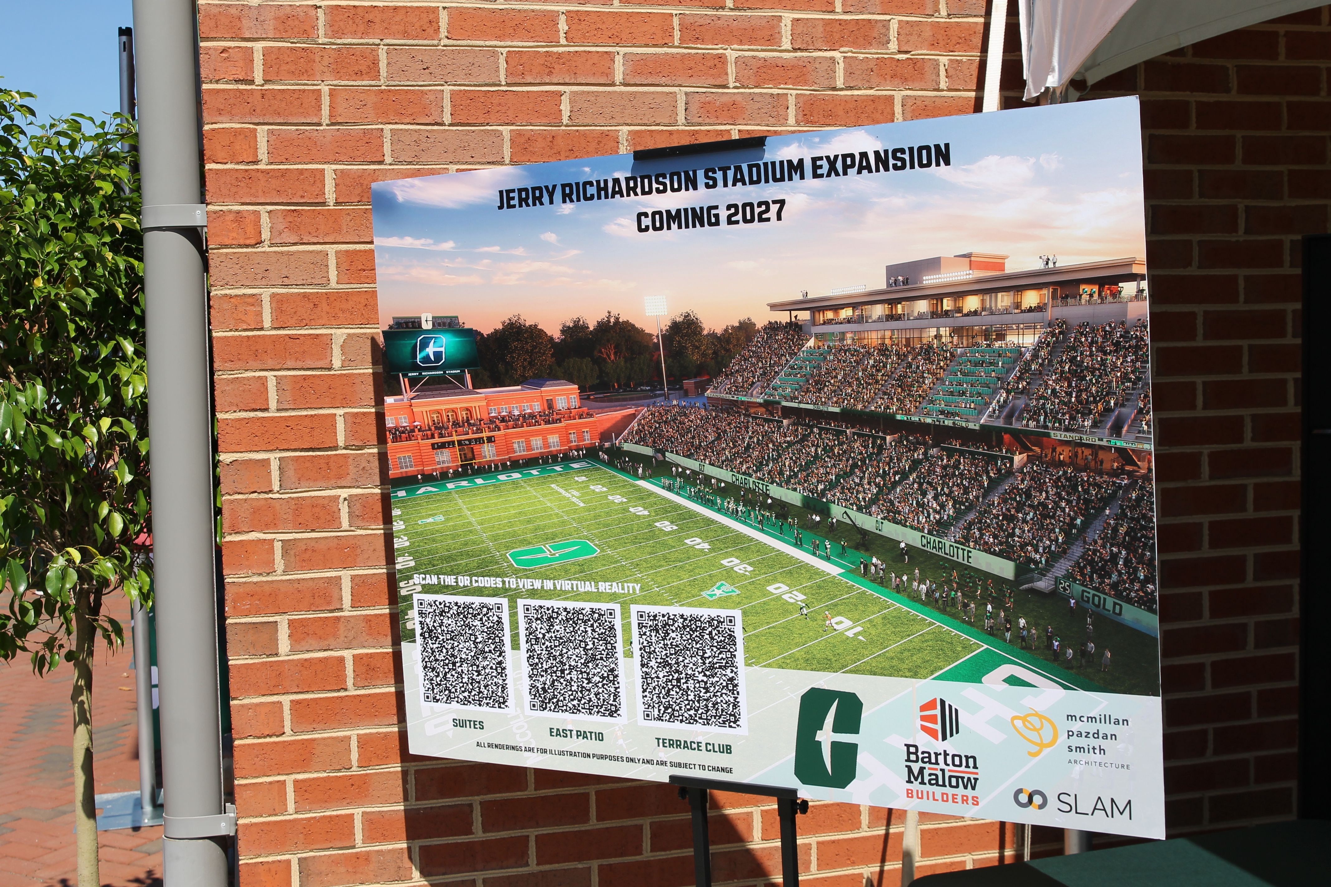 Poster on brick wall showing Jerry Richardson Stadium expansion plan with seats, field, and crowd. Text reads "Jerry Richardson Stadium Expansion Coming 2027" with QR codes for virtual tours.