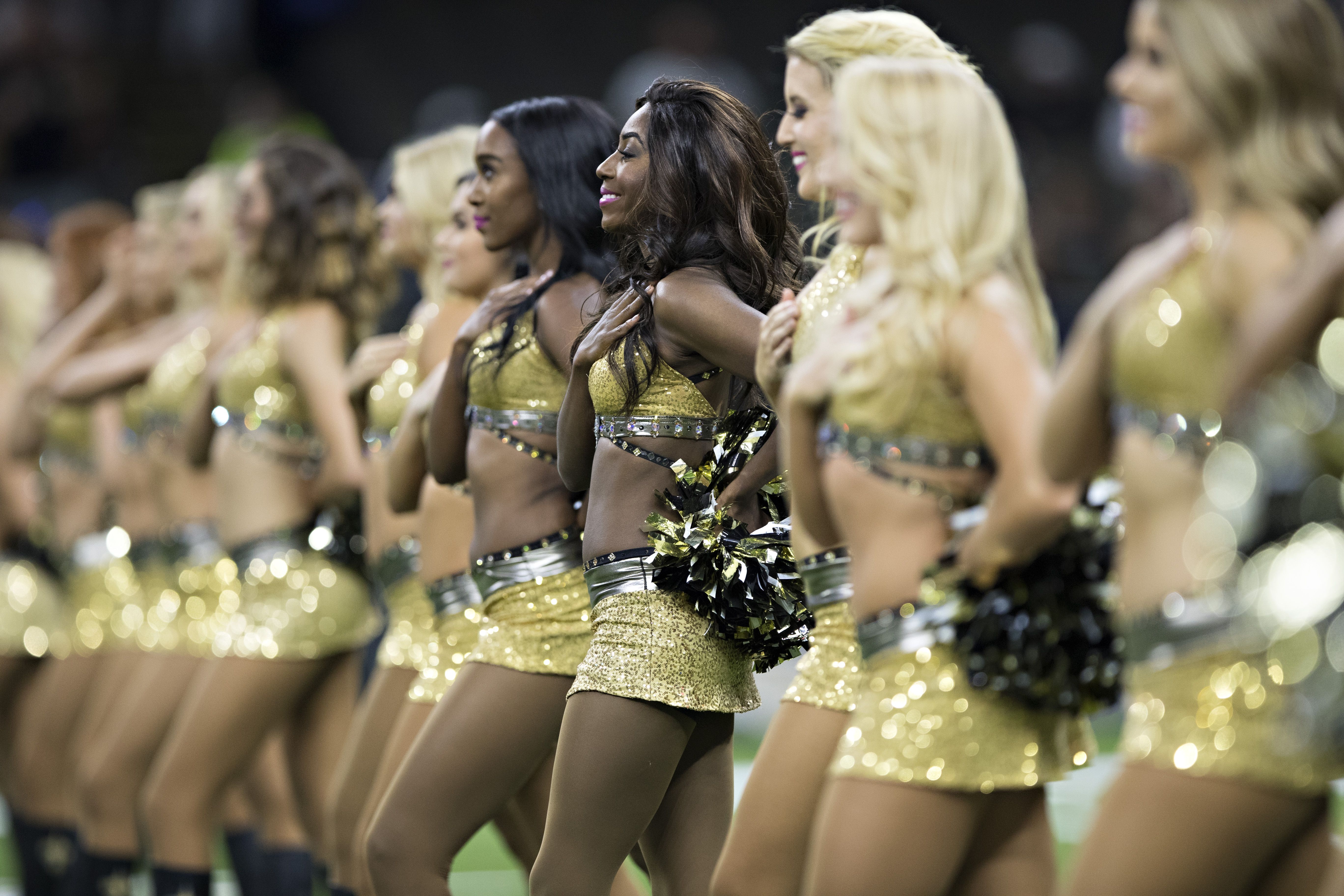 A line of Saints cheerleaders wearing gold uniforms cover their hearts and stand at attention.