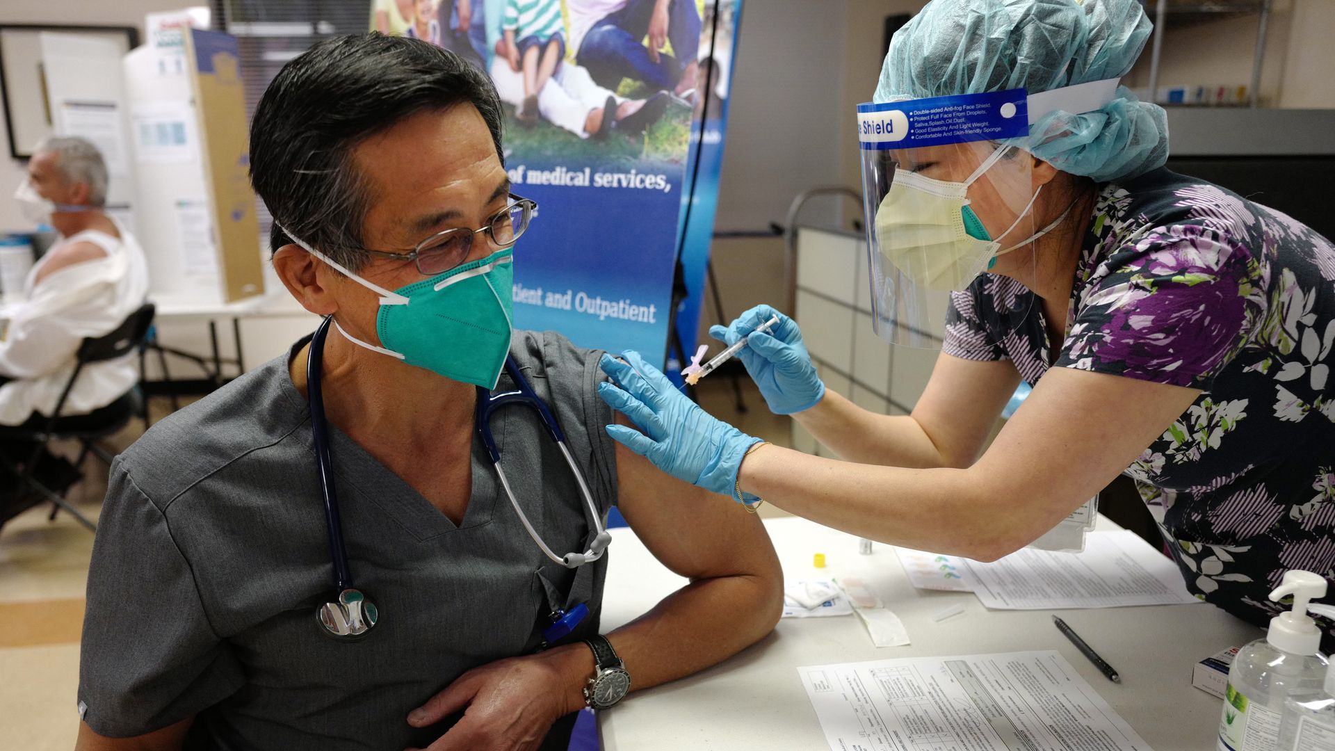 Photo of a masked doctor receiving the Pfizer vaccine from a masked nurse wearing gloves