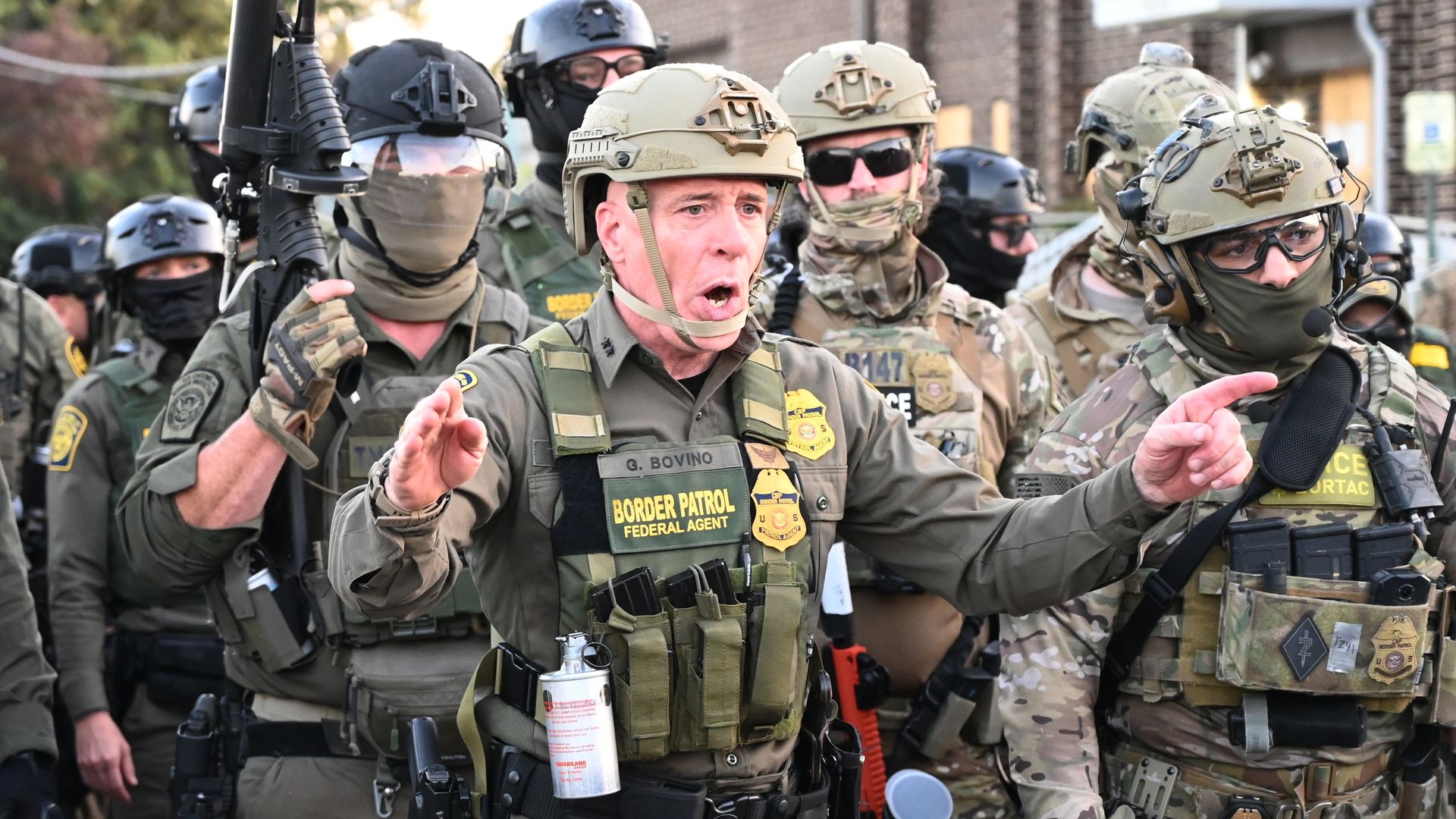 Photo of soldiers in fatigues holding guns while one commander shouts orders. 