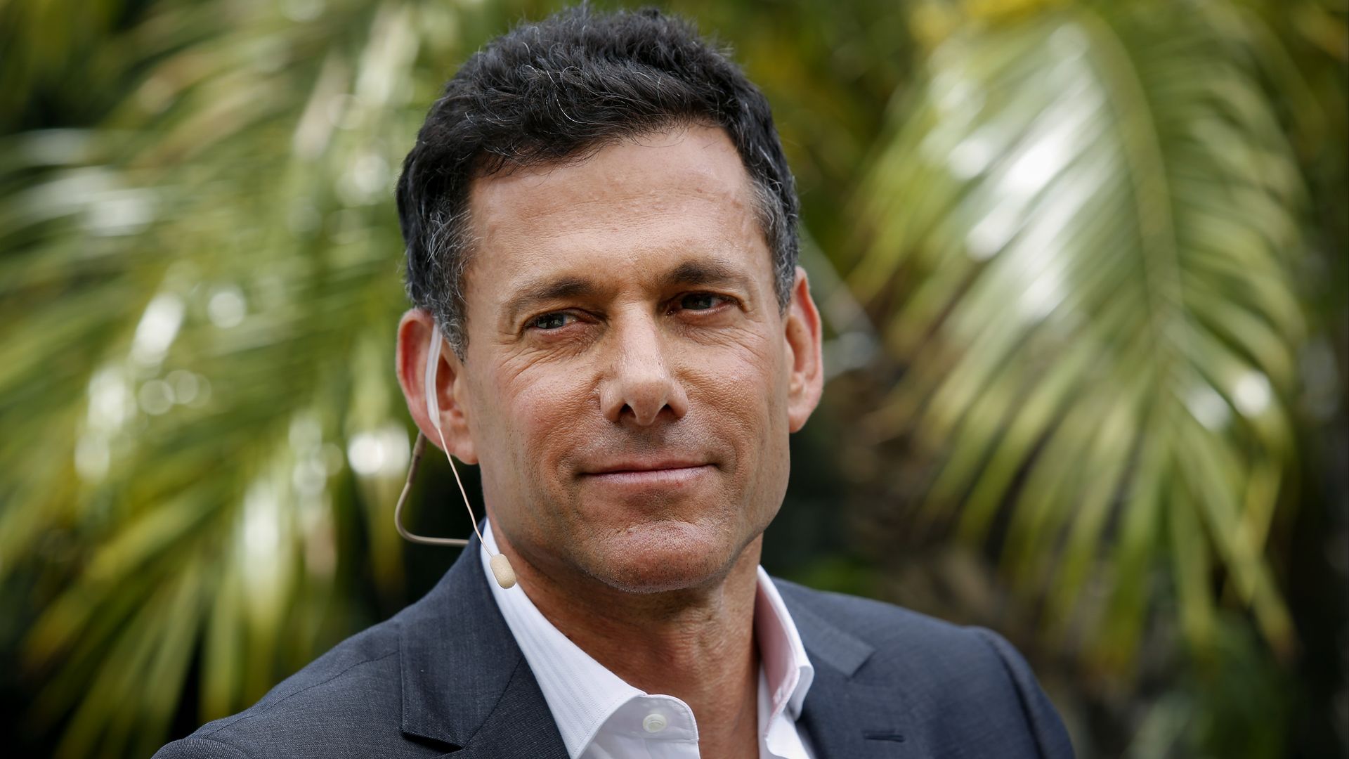 A man in a suit, white shirt with no tie, photographed from the shoulders up