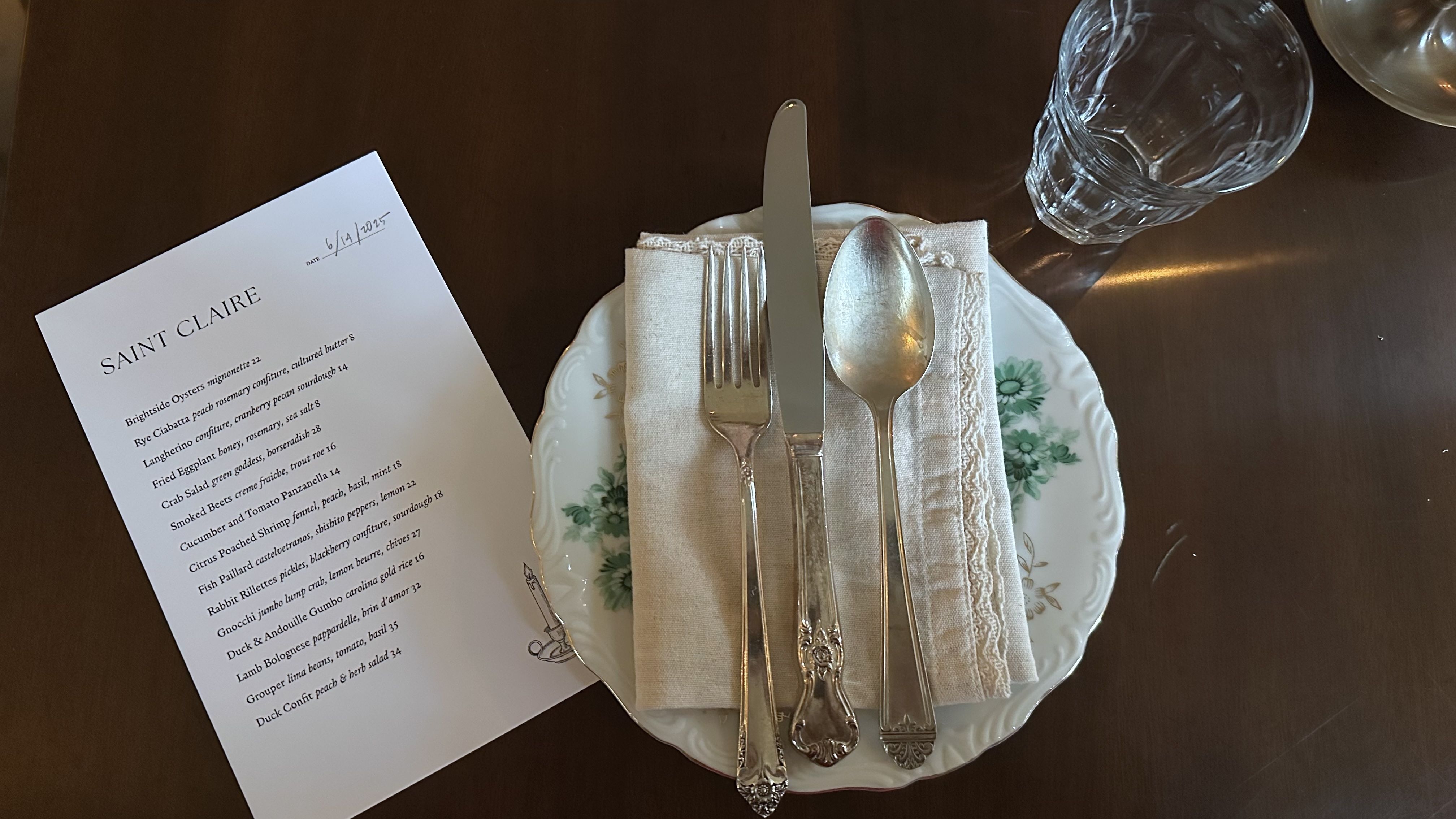 A menu sits next to a porcelain plate with a knife, spoon and fork.