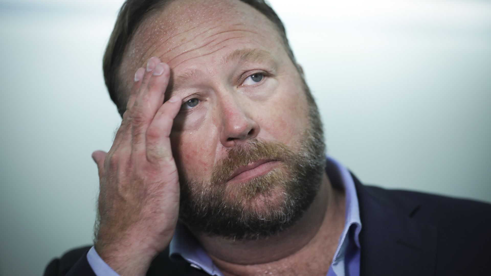 Photo of Alex Jones wiping his face with his right hand