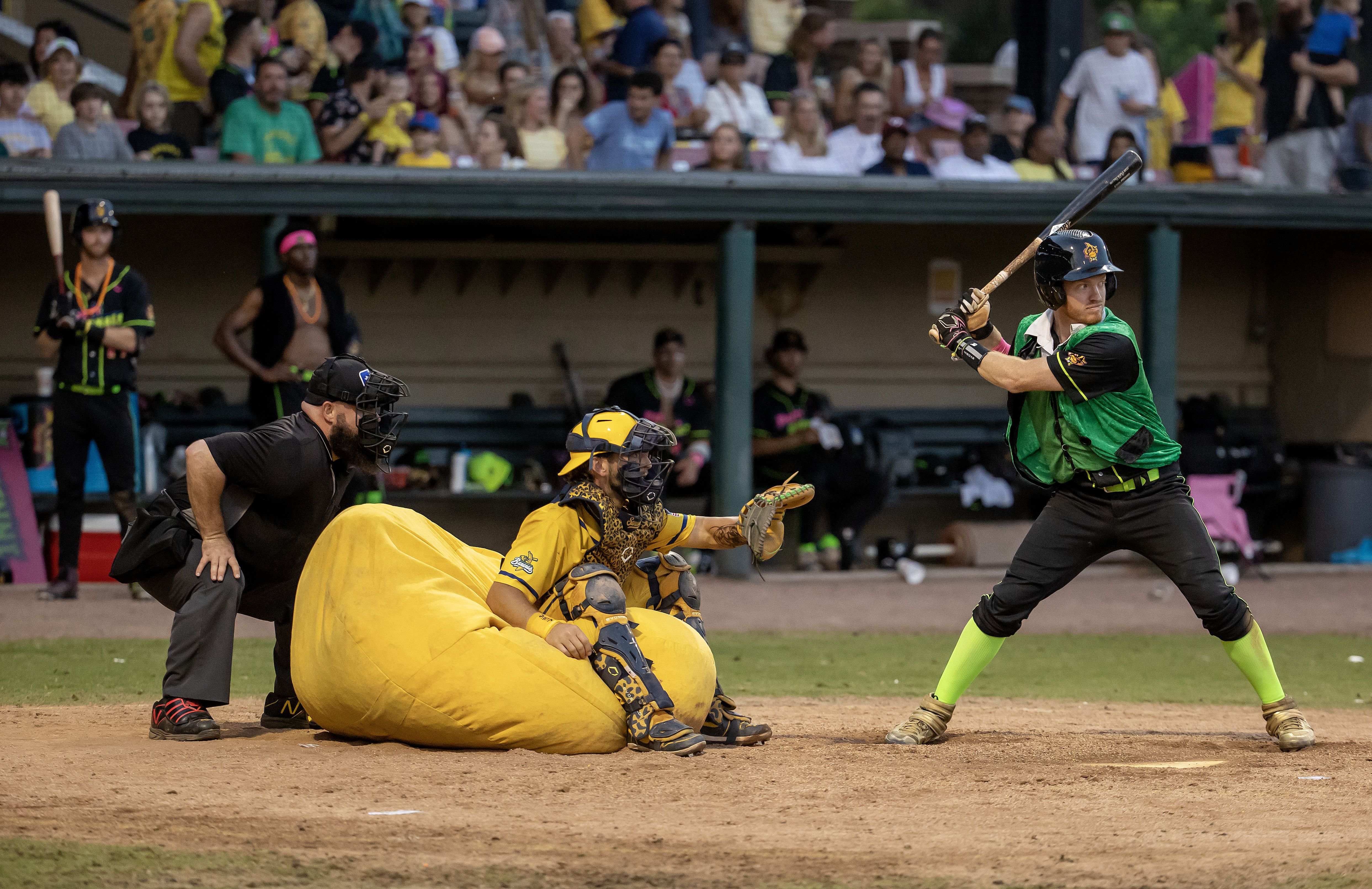 An umpire, a catcher sitting in a beanbag chair and a hitter with a bat.