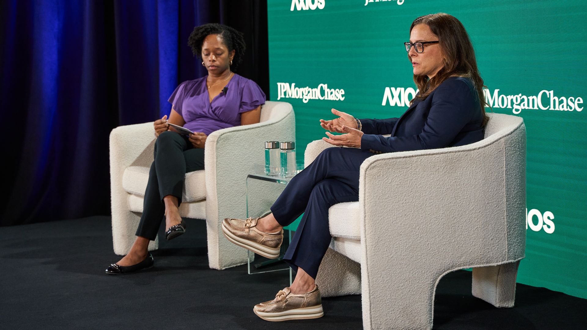 Axios' Kristal Dixson speaks with Partners for HOME CEO Cathryn Vassell in front of a green sign that says "AXIOS" and "JPMorganChase"