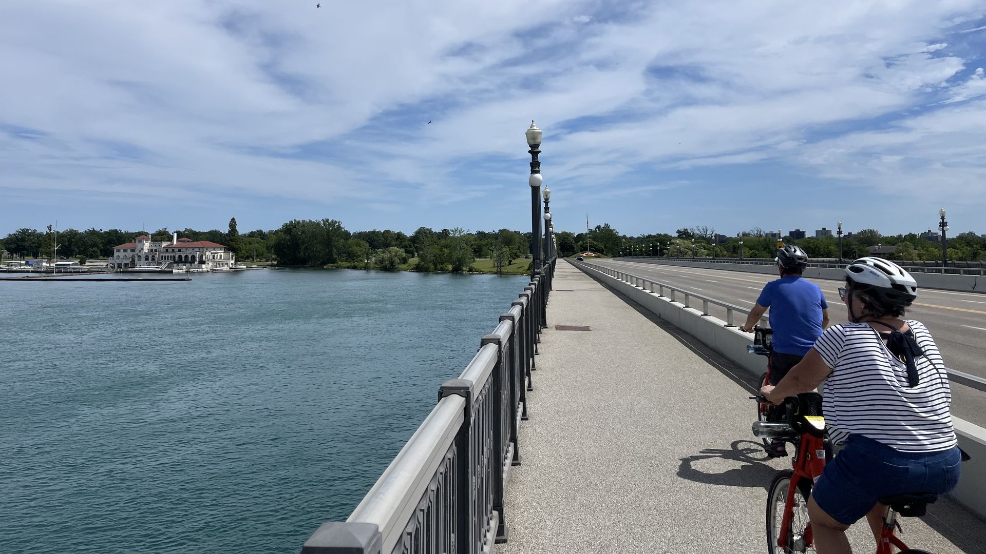 Two cyclists ride toward Belle Isle over the Detroit River.