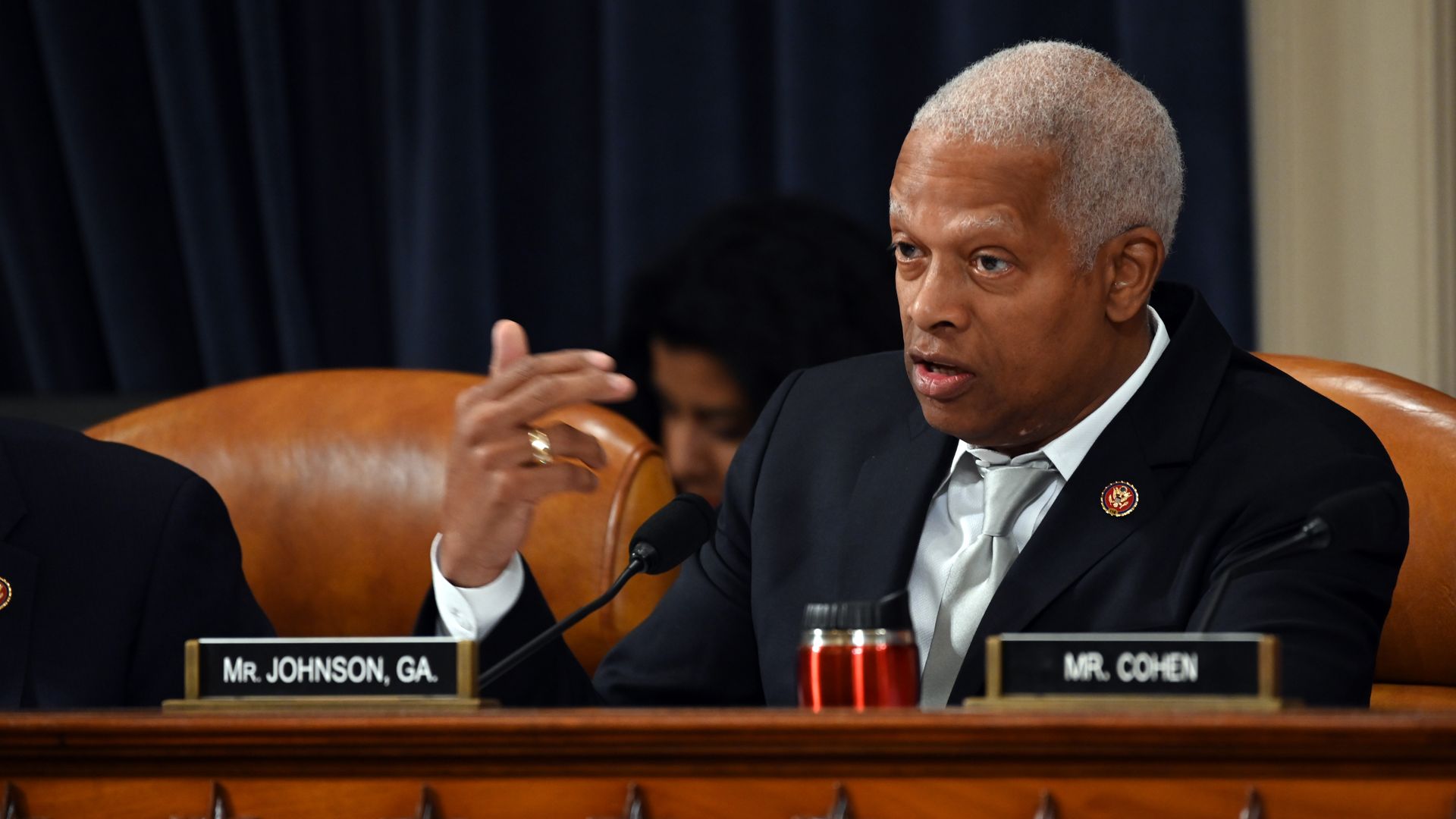 Hank Johnson sits at a dais in a congressional chamber and speaks to an off-camera person