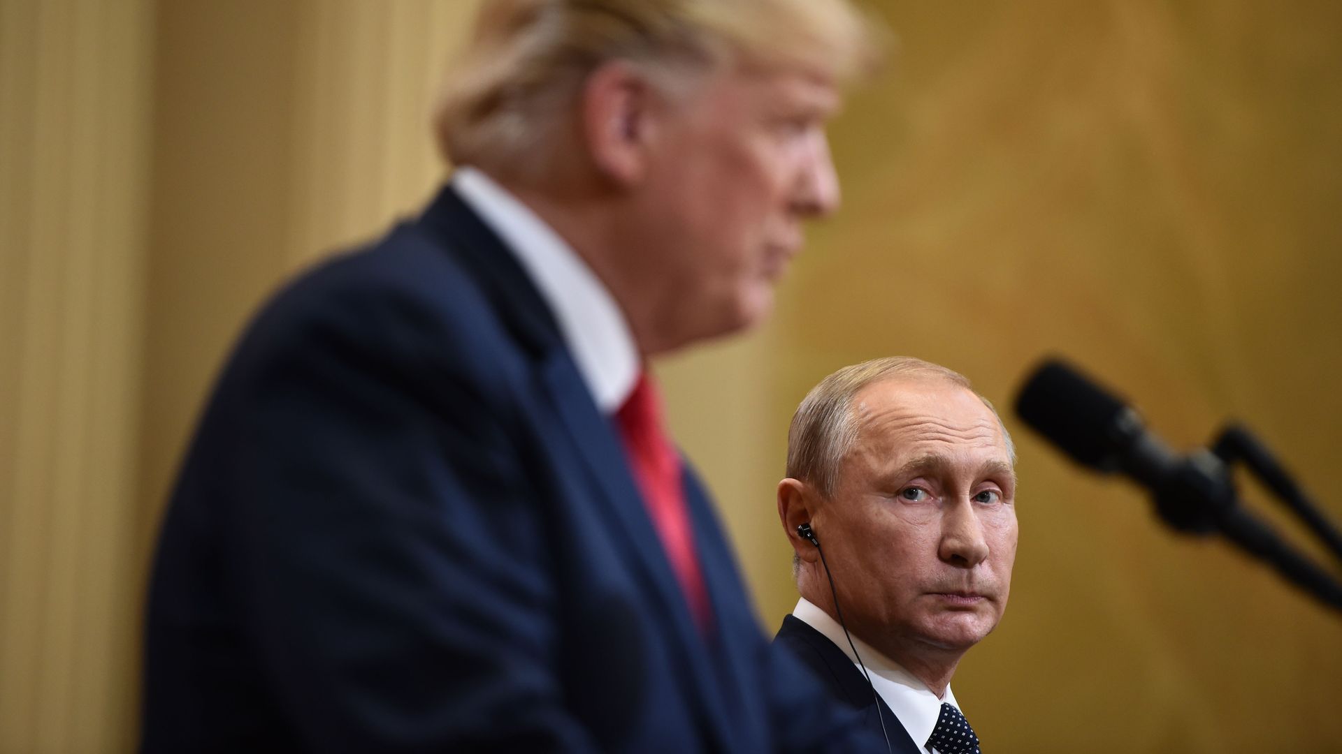 Vladimir Putin in background in focus looks concernedly at Trump, in foreground, blurry.