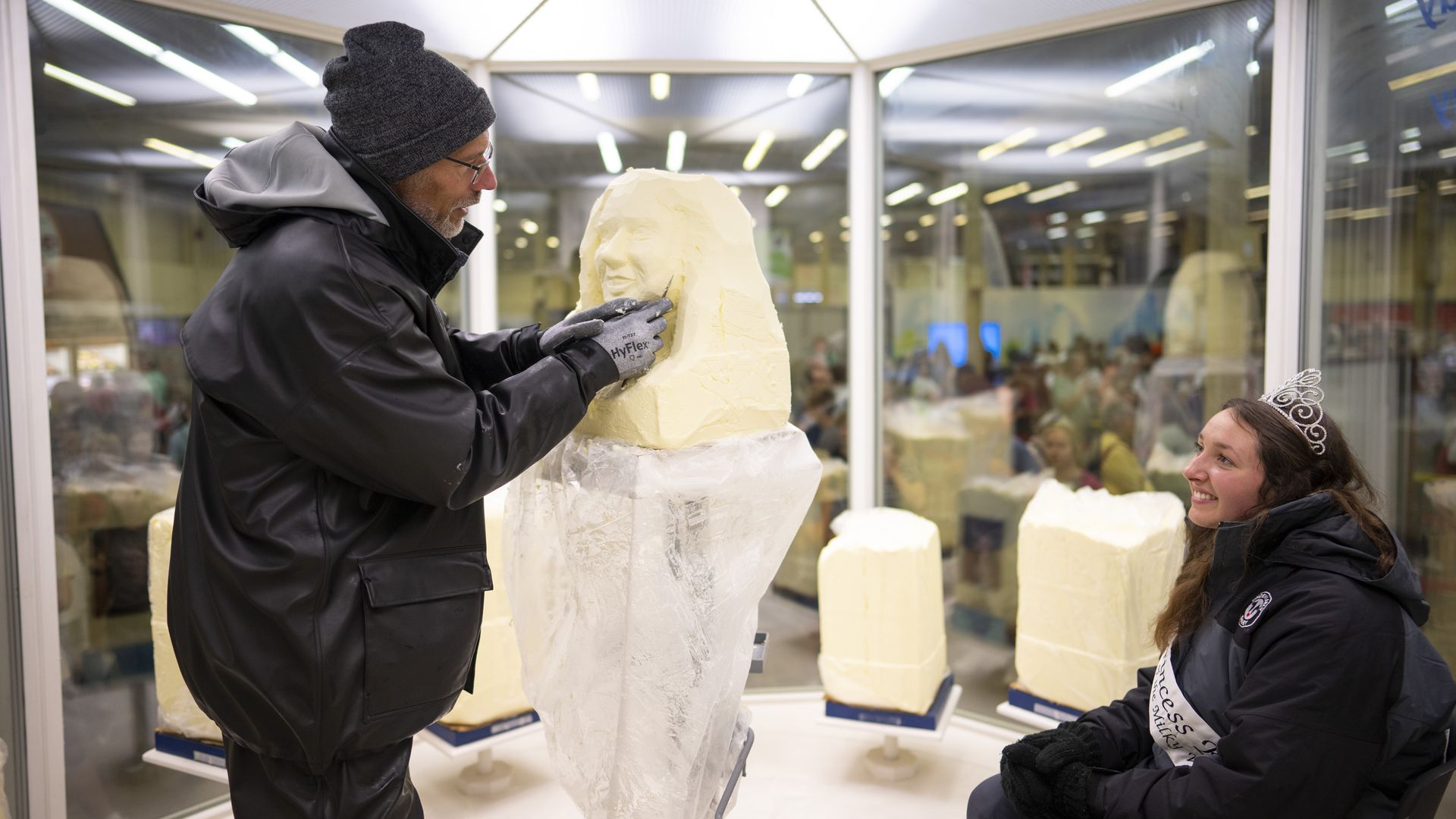 A man carving a large block of butter in the shape of a woman's head.