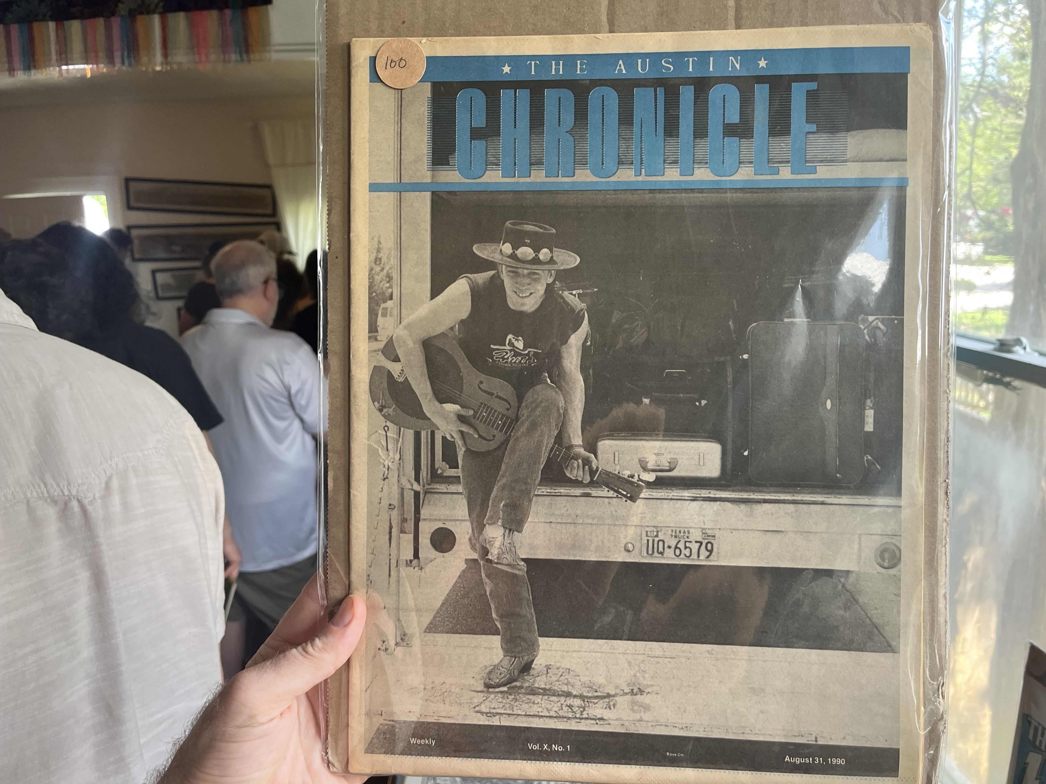 Vintage magazine cover with the title "The Austin Chronicle" in a blue banner; black-and-white photo of a man in a hat playing an electric guitar, leaning forward, and a round sticker reading 100 at the top left.
