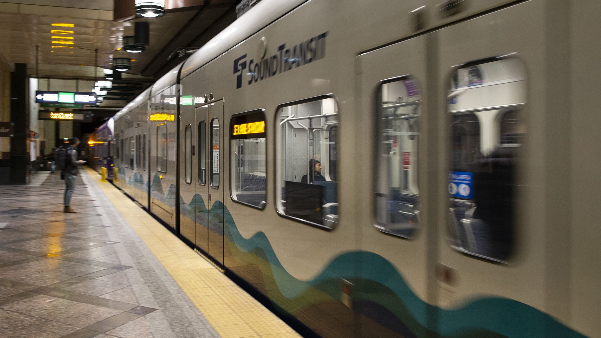A Sound Transit train moves in a blur away from a platform.