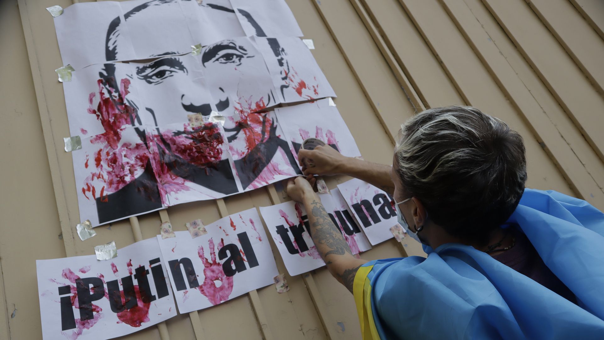 Photo of a person reaching for a large poster with Putin's face and red handprints all over it