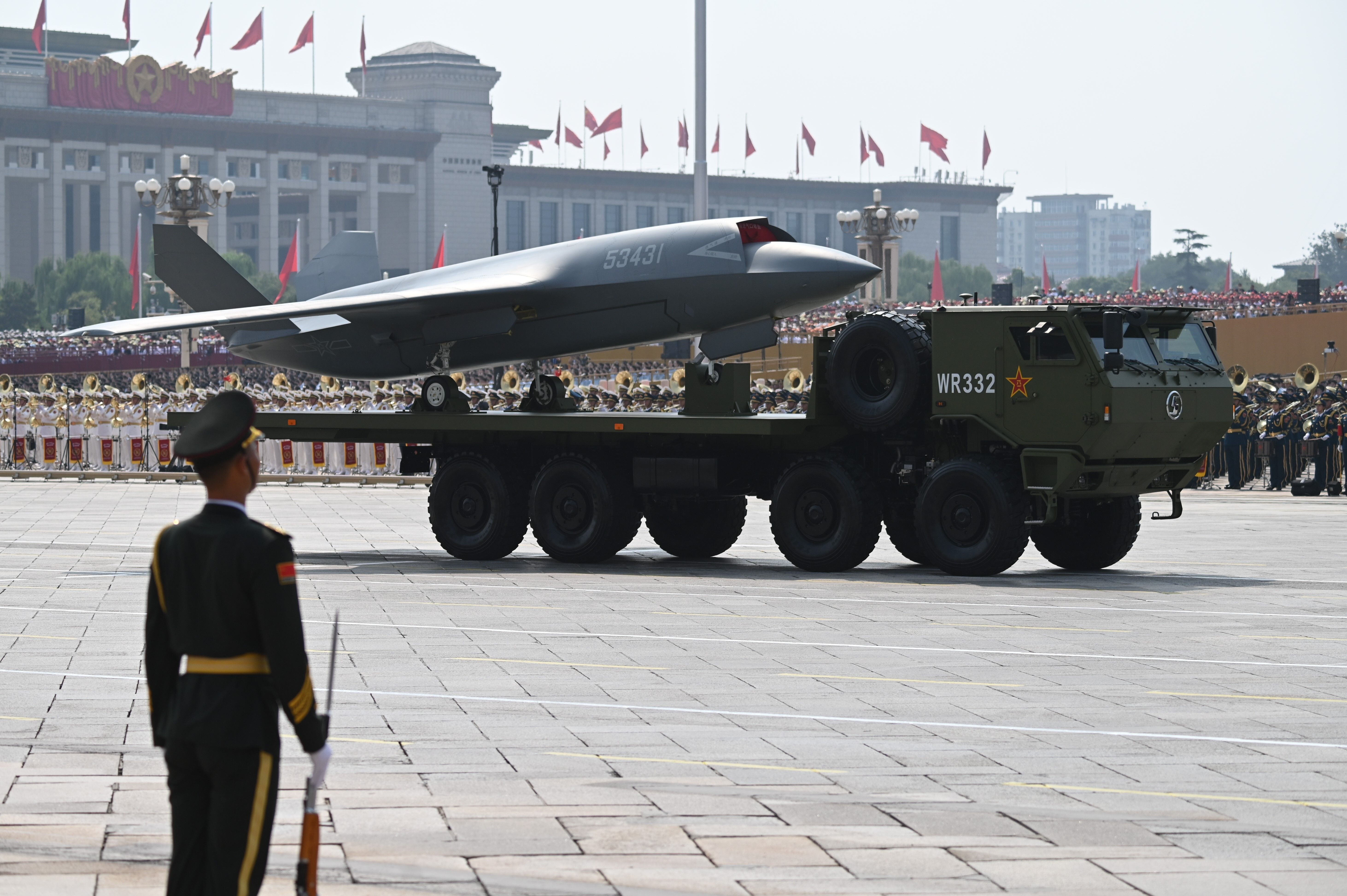 An unmanned black military aircraft sits on a green military transporter.