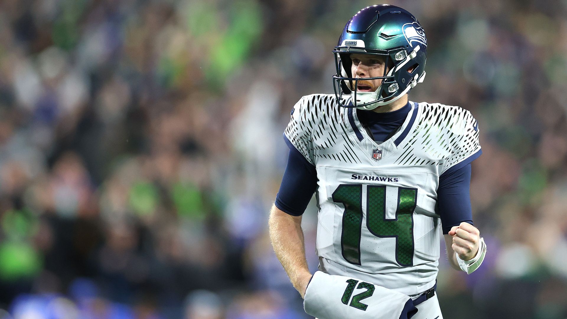 A football player in a uniform of silver white, navy and green looks happy after a touchdown. 