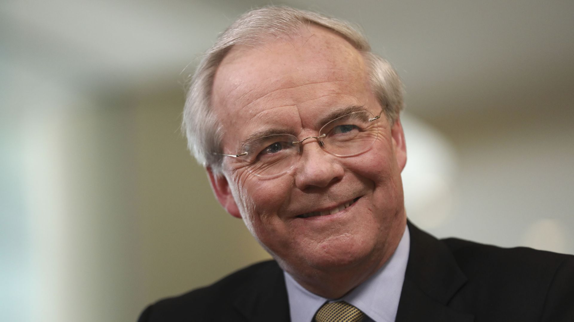 A person in a dark suit and tie and glasses
