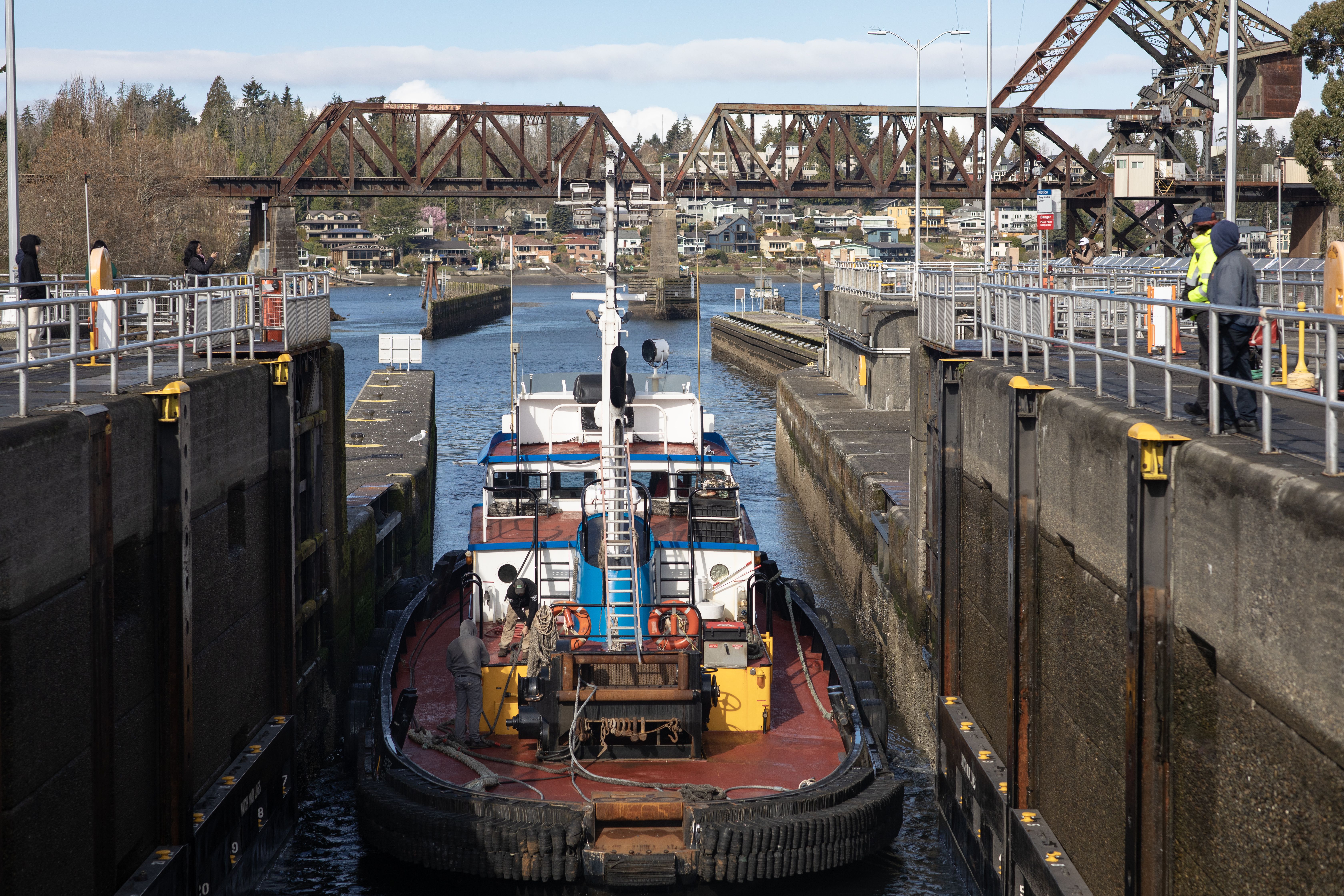 A commercial-looking boat sits on the water in the Ballard Locks, with concrete walls on both sides and a bridge in the distance.