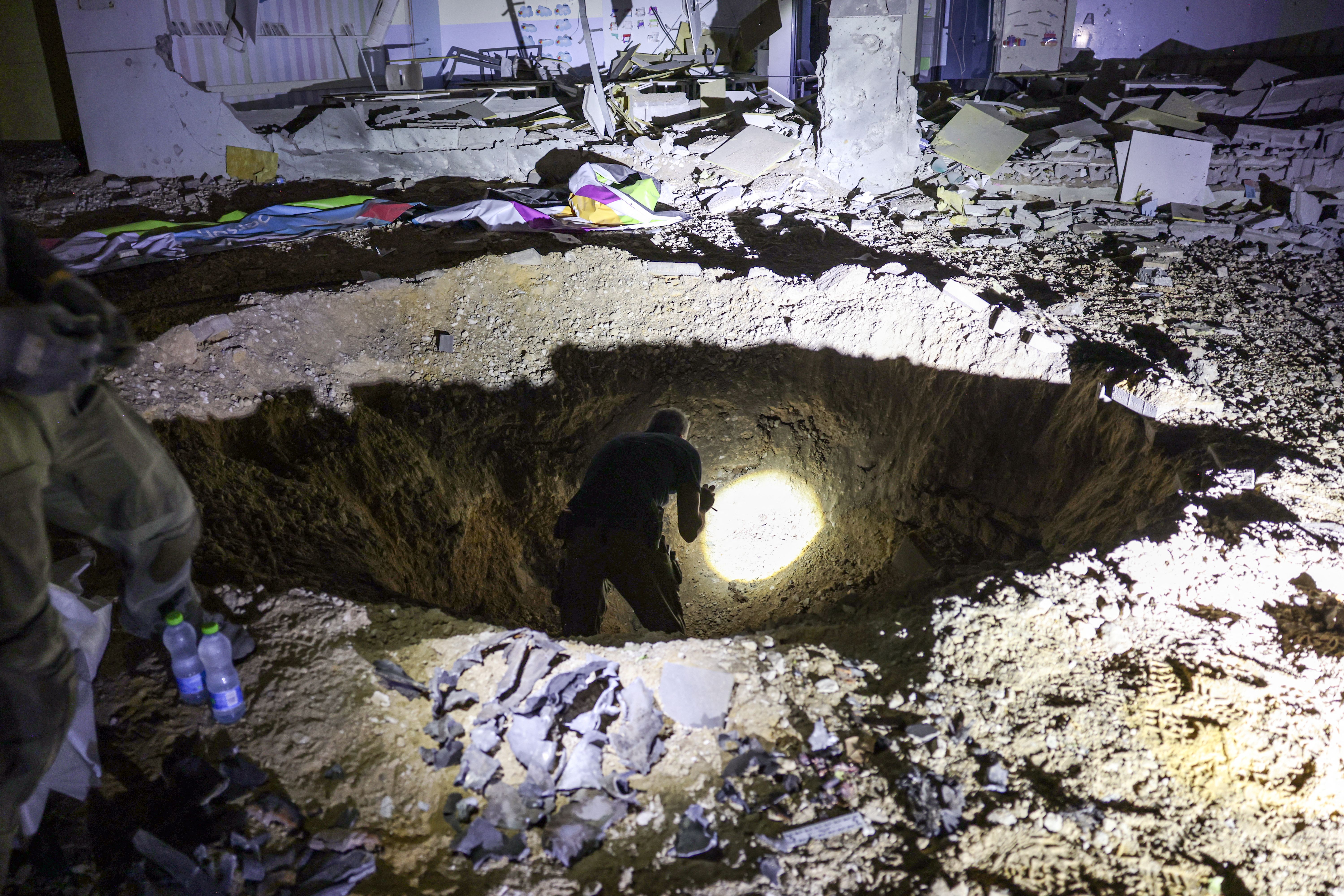 Israeli authorities inspect a crater left by an exploded projectile at a heavily-damaged school building in the southern city of Gedera yesterday.