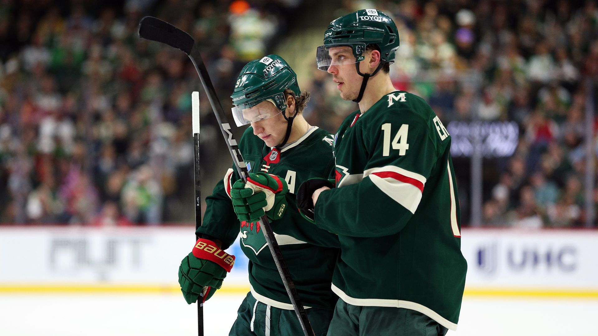 Two hockey players in green jerseys confer on the ice during a game