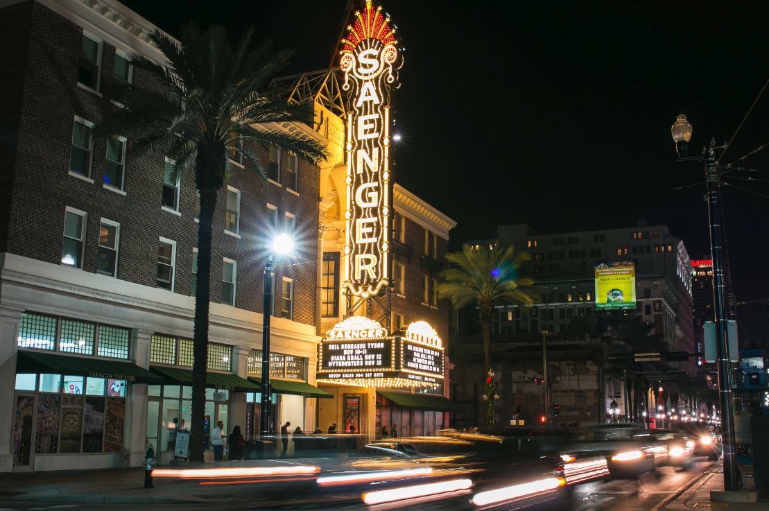 Photo shows the exterior of the Saenger Theater at night with blurred headlights on the street.