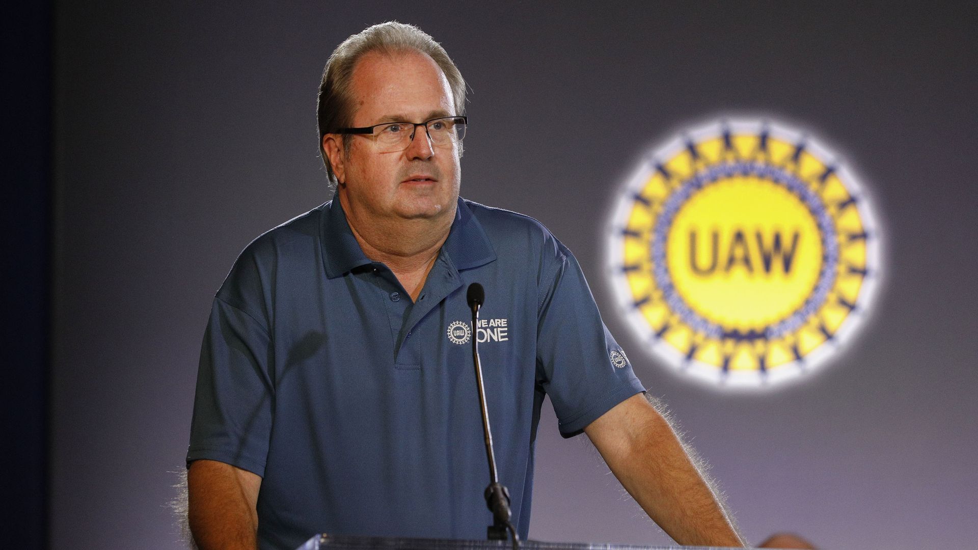 In this image, UAW president stands in front of a clear plastic podium.