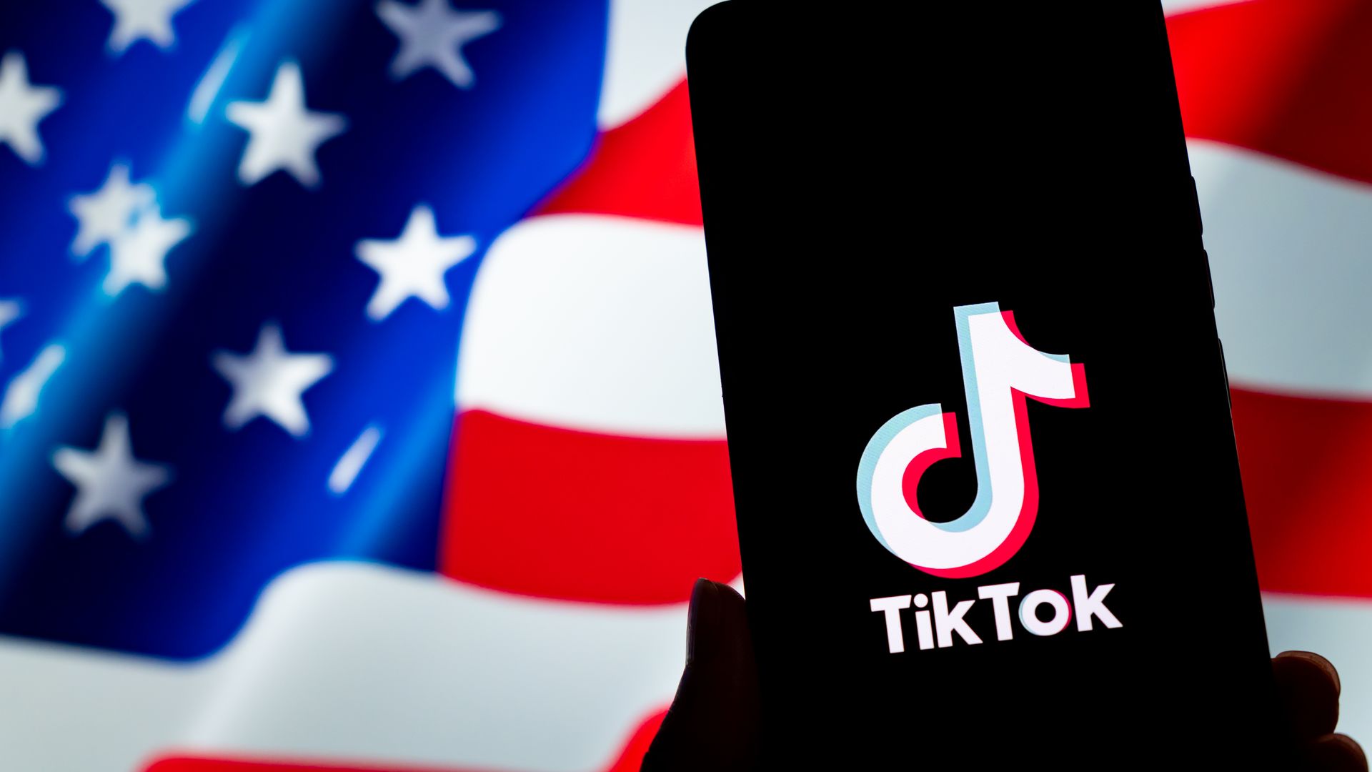 An silhouette of a phone with the TikTok logo in front of the American flag