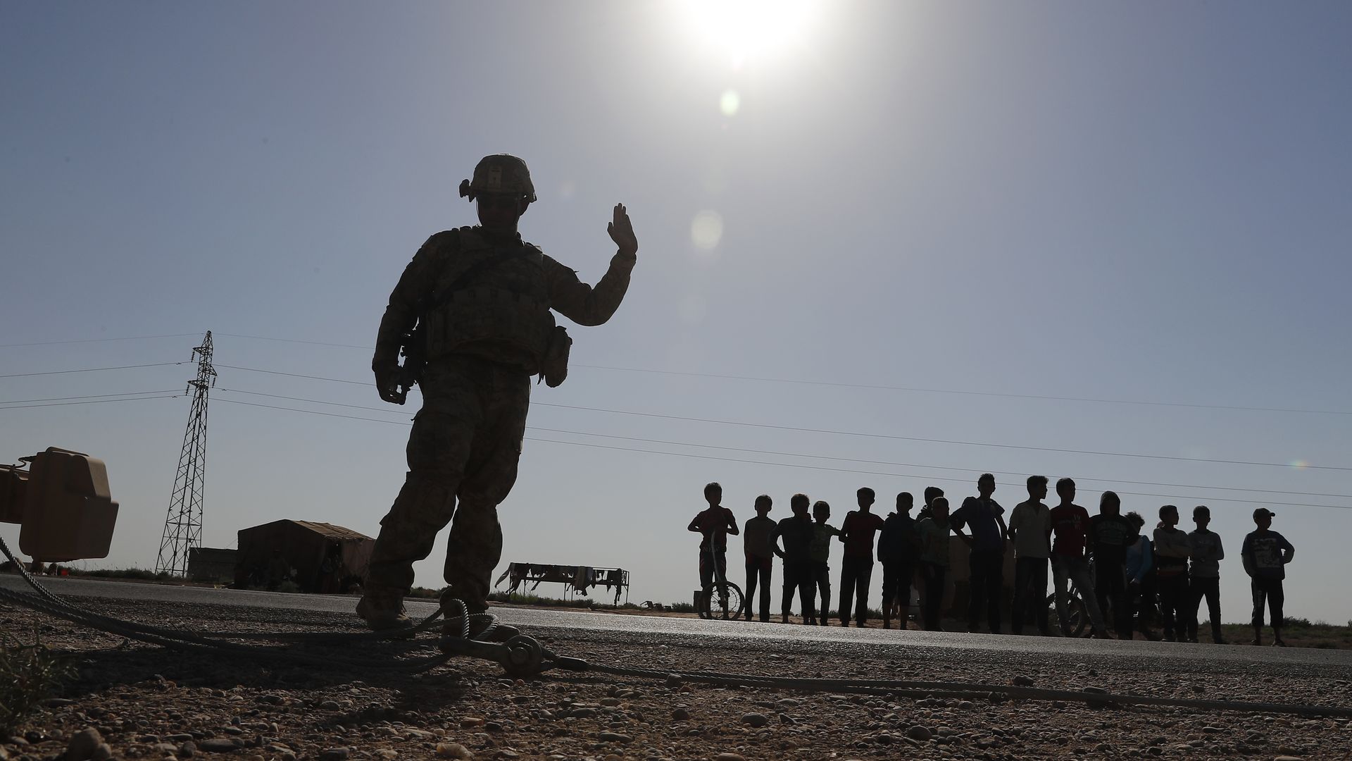 A U.S. silhouetted soldier, left, directs his armored convoy as Syrian children, background, watch, on a road that links to Raqqa city, northeast Syria. 