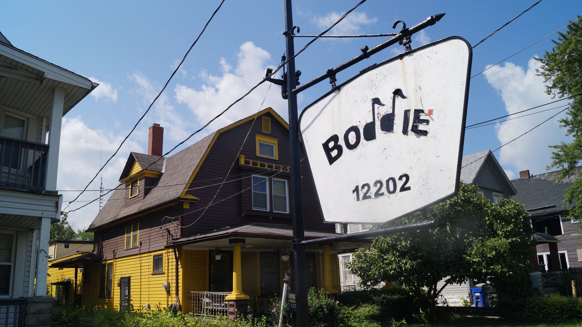 A white hanging sign reading "Boddie, 12202" in front of a brown and yellow house. 