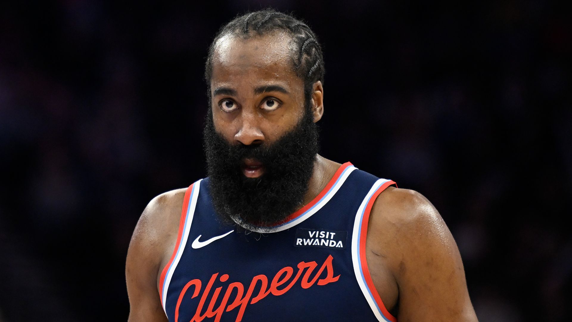 James Harden's bearded face while wearing a navy blue Clippers jersey. 