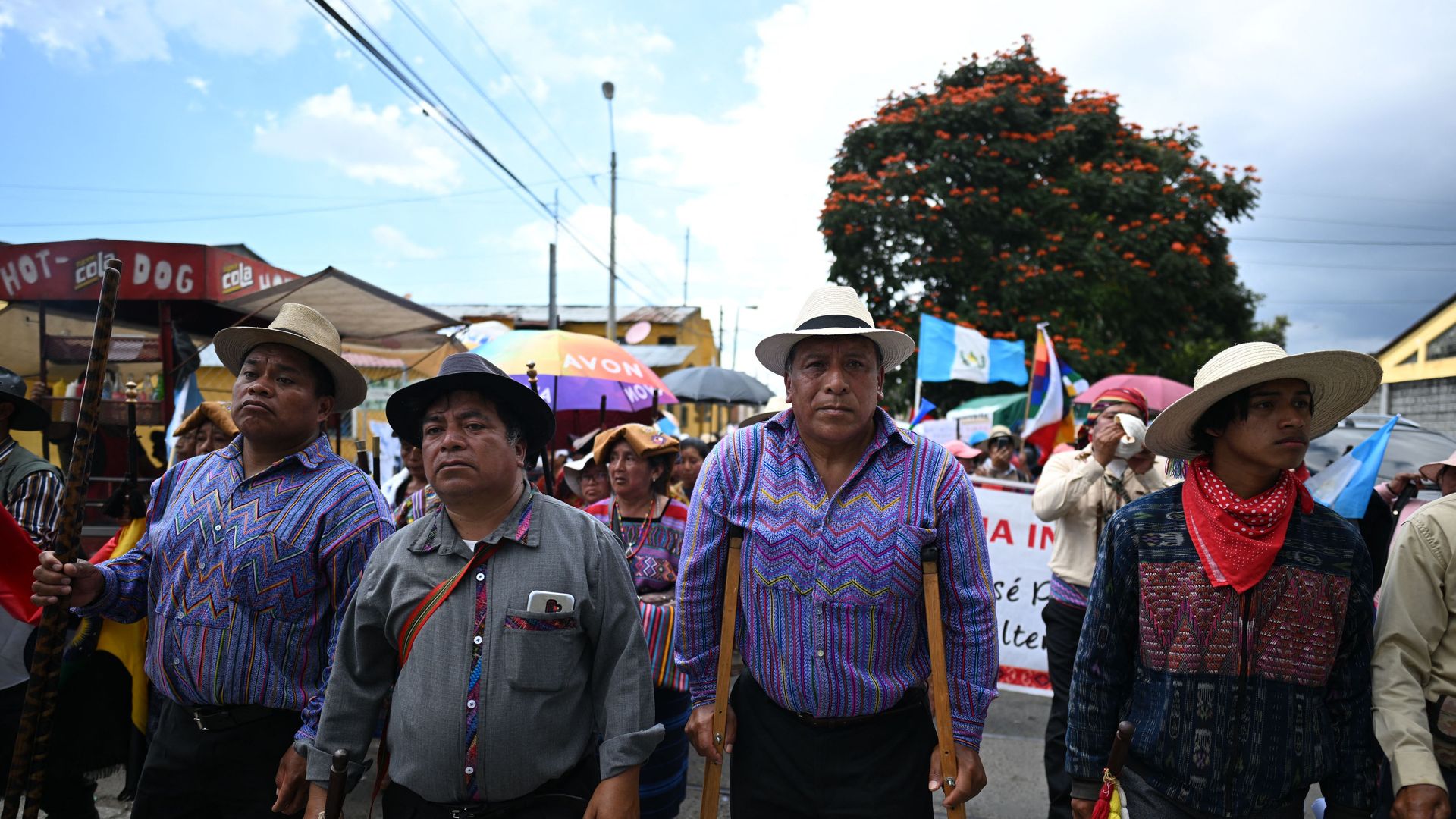 Three Guatemalan Kakchiqueles indigenous men and a teen boy march during a sunny day in Guatemala. One man is walking on wooden crutches. 