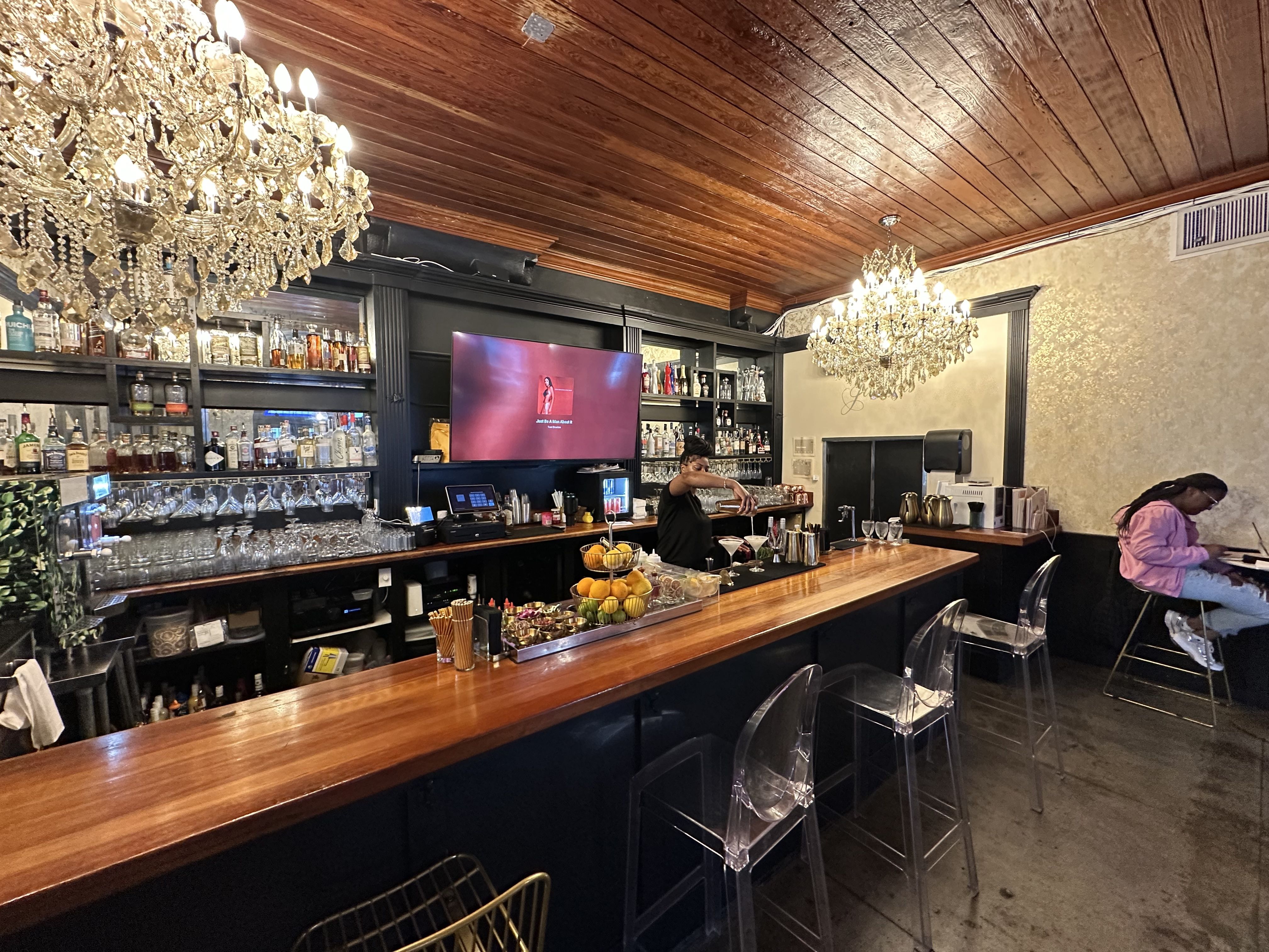 A woman pours a cocktail at a chandelier-topped bar.