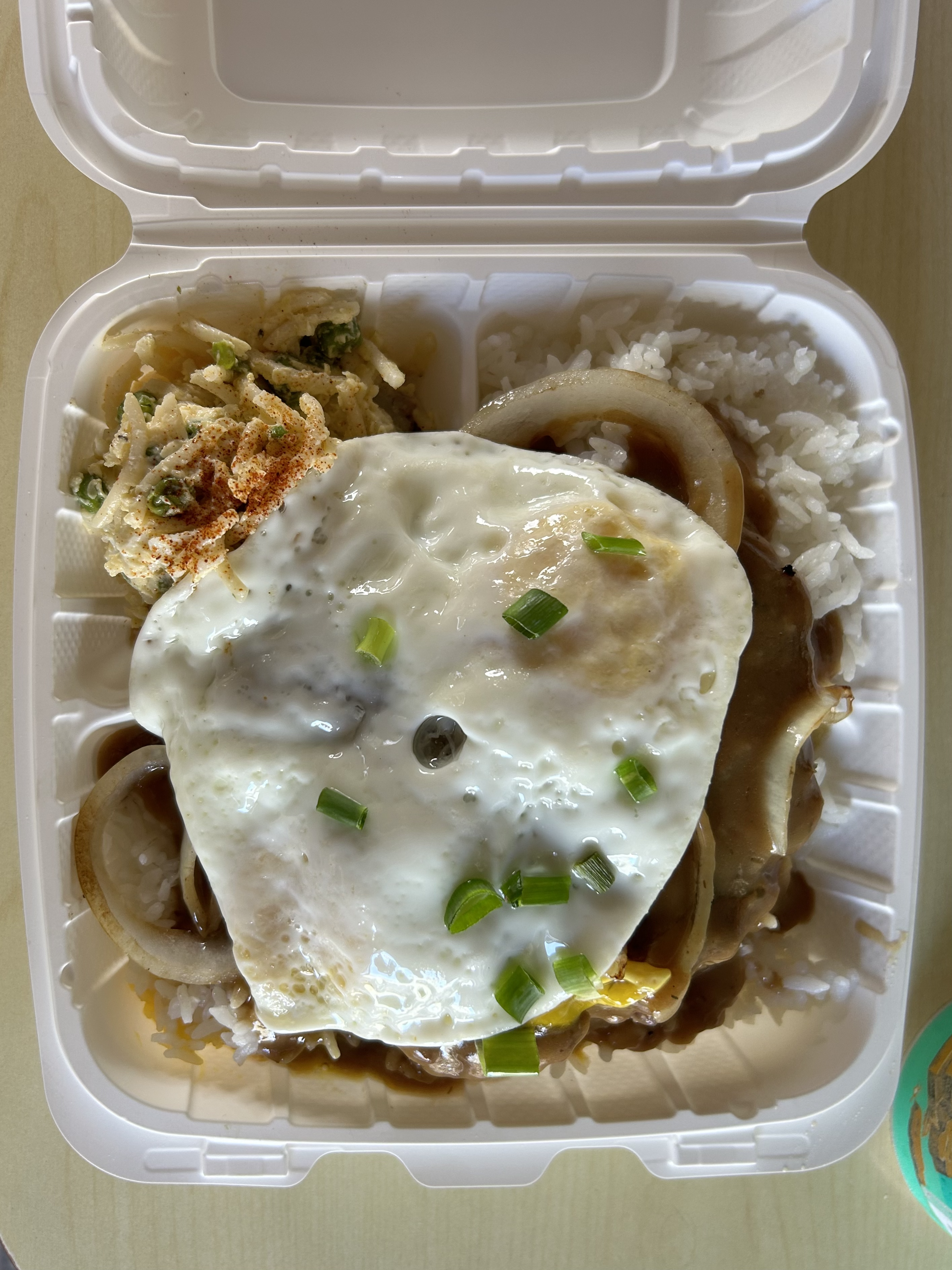 Photo of a plate of loco moco, with fried egg on top of onion, beef patty and rice