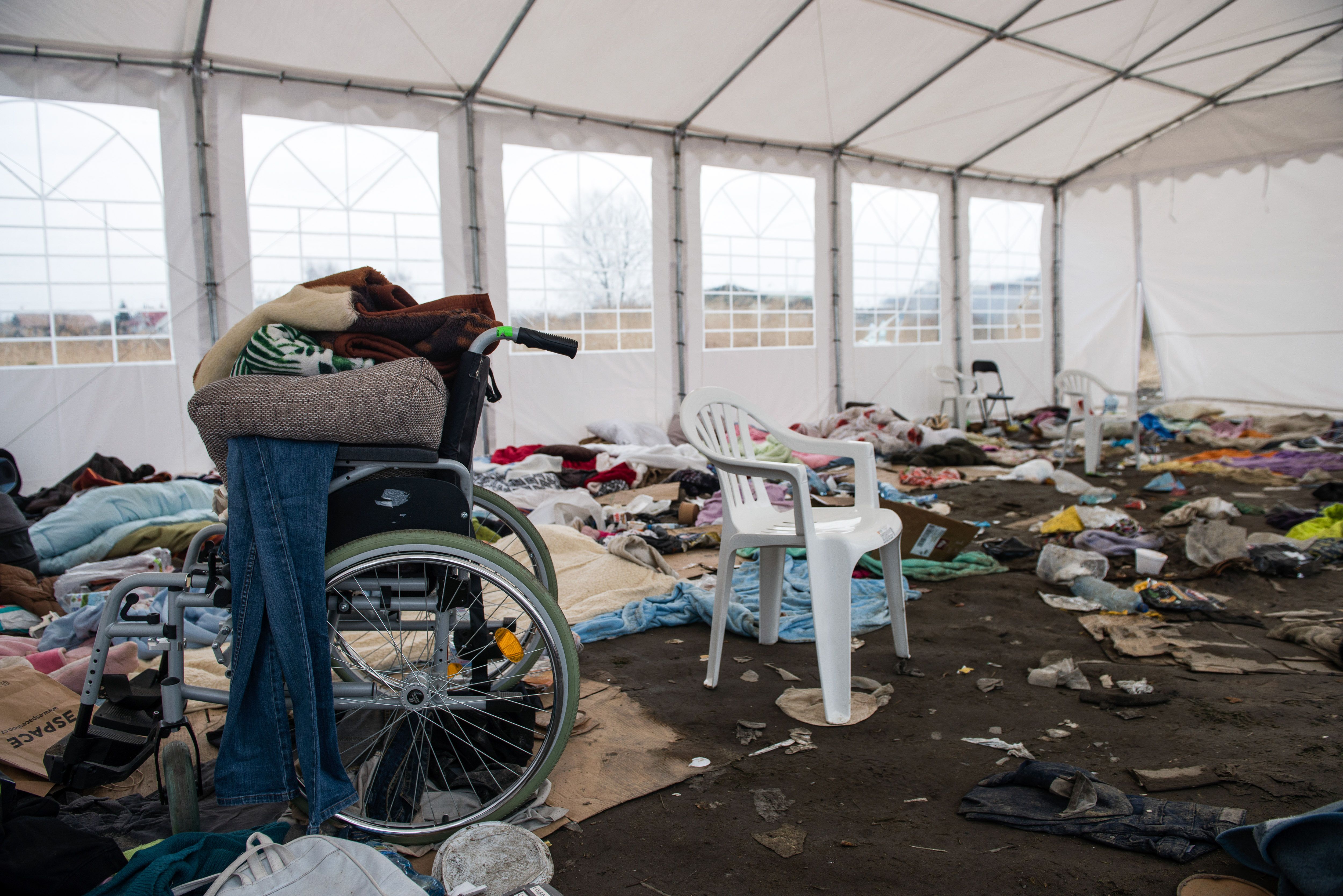 Photo of a space littered with clothes bedding and a wheelchair