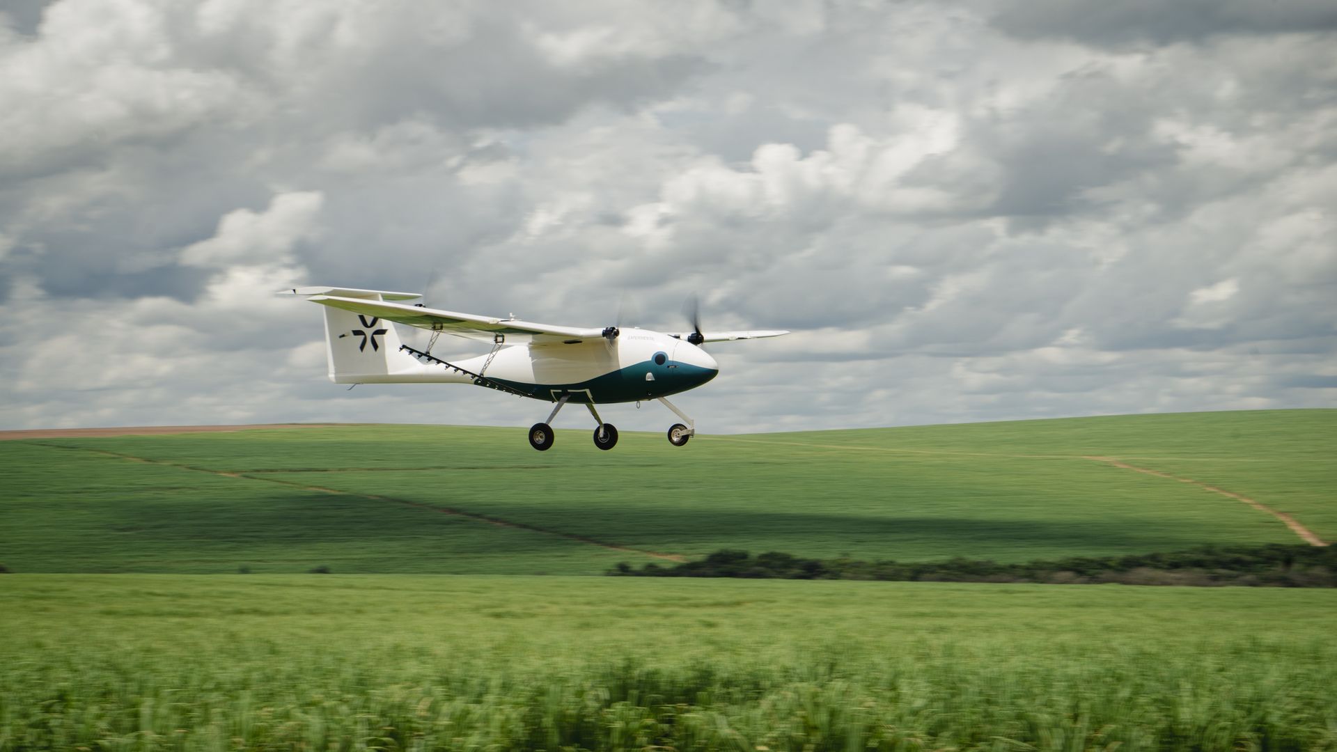 A Pyka pilotless airplane flies above green crops.