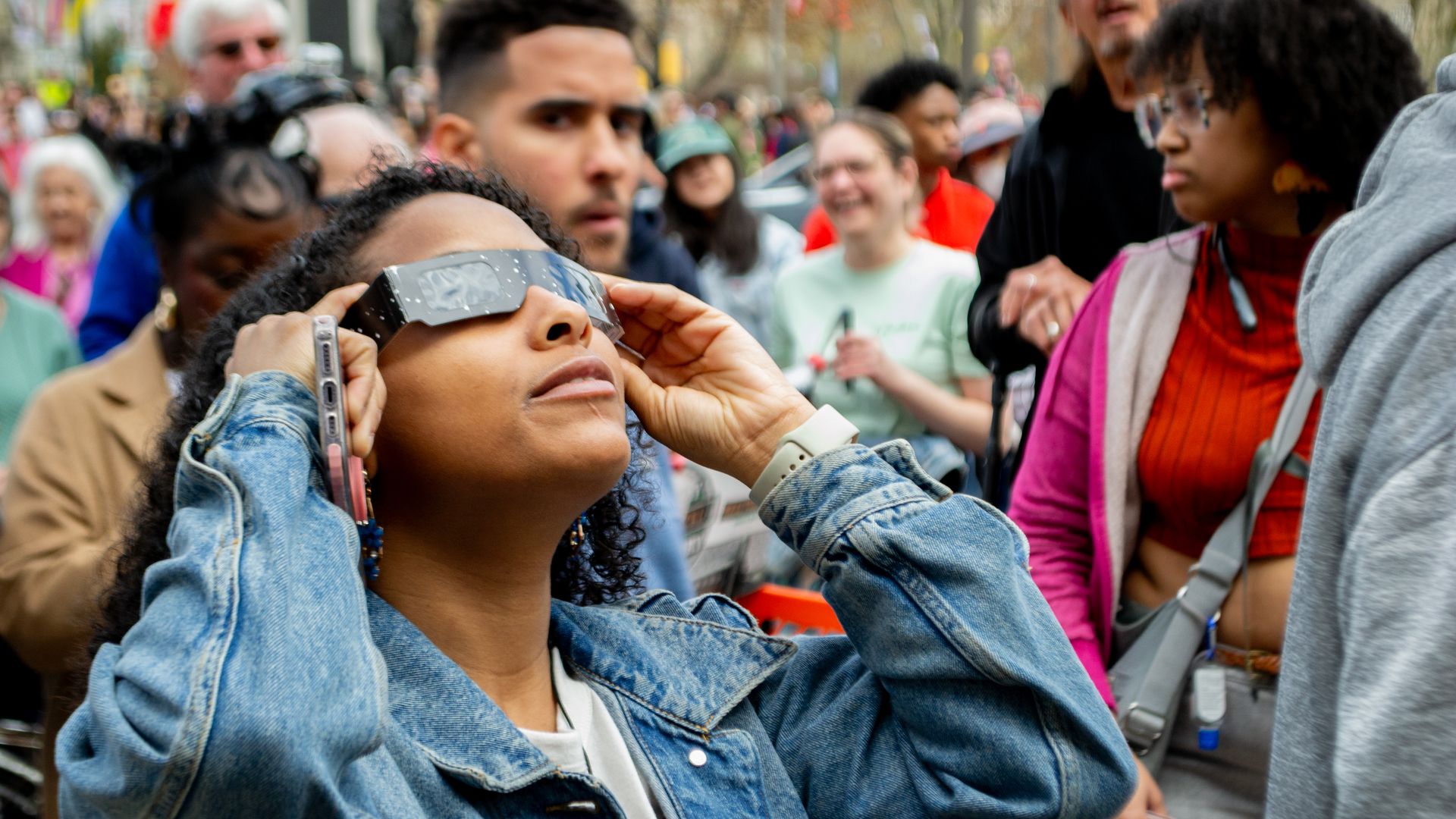 Person wearing eclipse glasses looking up in a crowd.