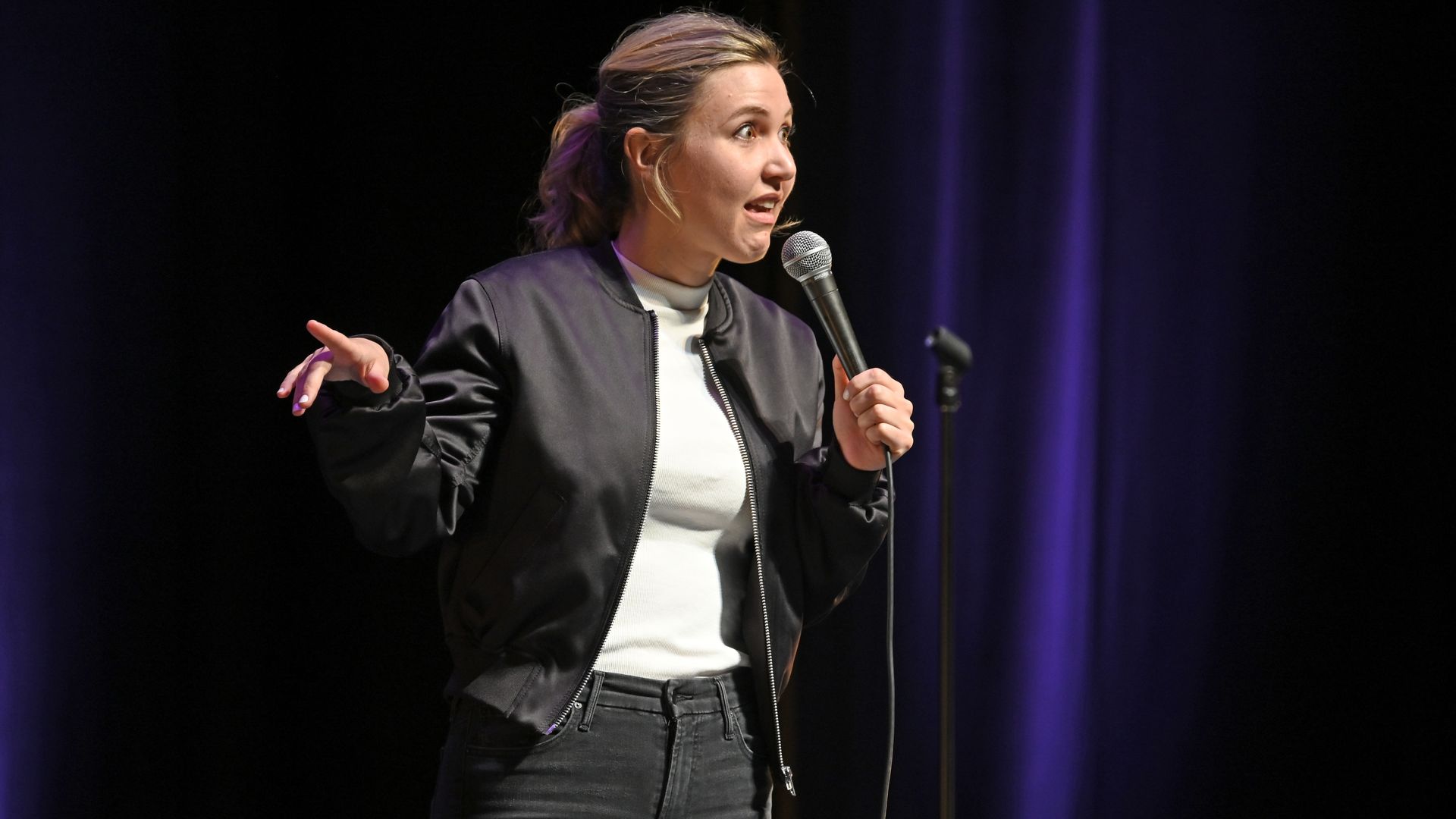 Taylor Tomlinson performing standup in a black jacket