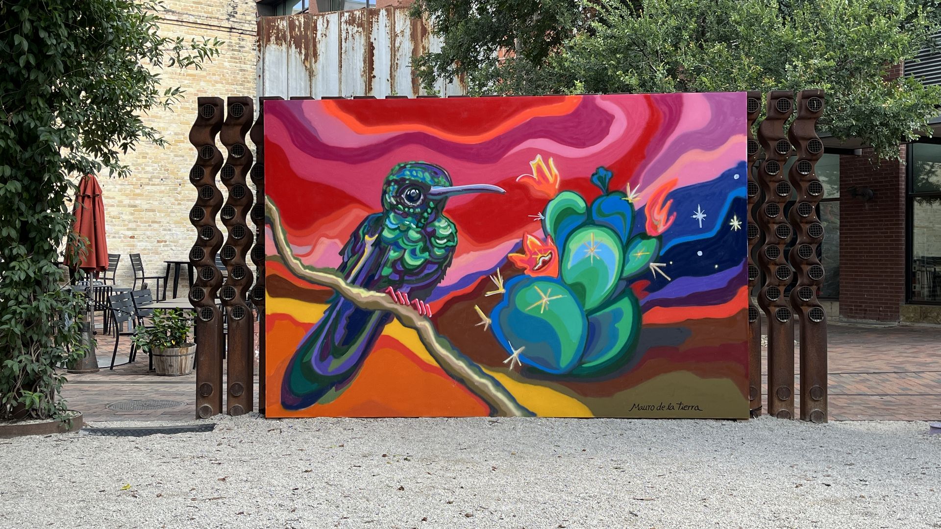 An outdoor mural depicting a colorful hummingbird perched on a cactus. 
