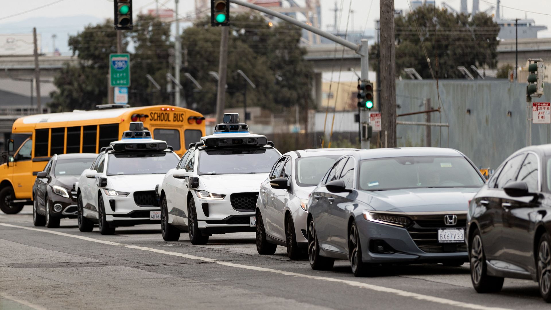A line of traffic, including two Waymo robotaxis, and a school bus, on a busy urban street in San Francisco.