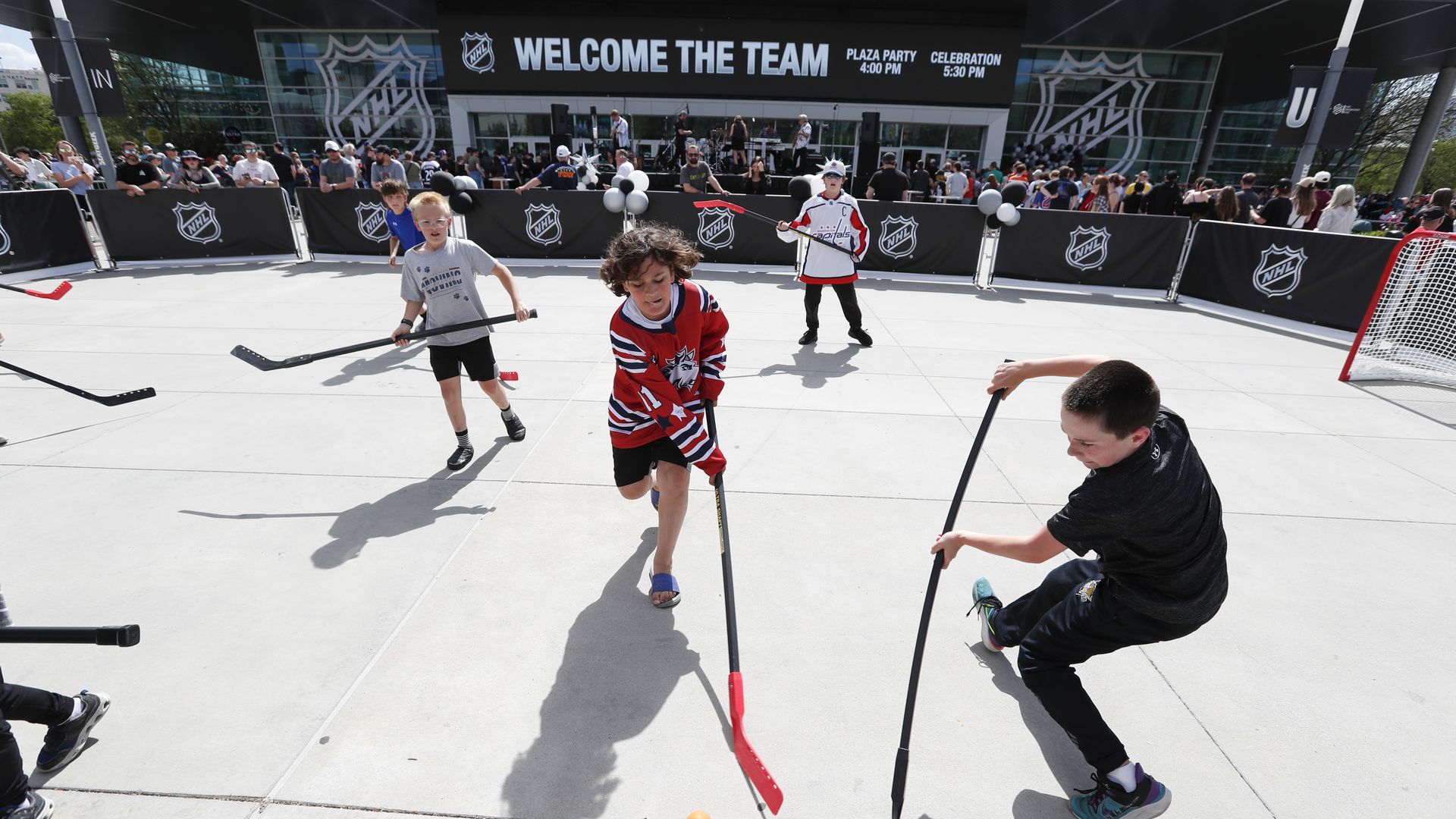 Children play stick hockey in front of the Delta Center.