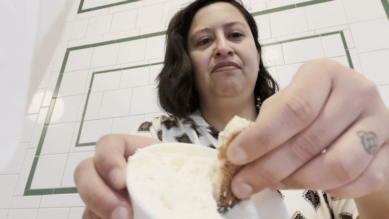 A gif of Axios Boston's Steph Solis dunking a piece of an everything bagel from PopUp Bagels into a container of their Parmesan-garlic cream cheese.