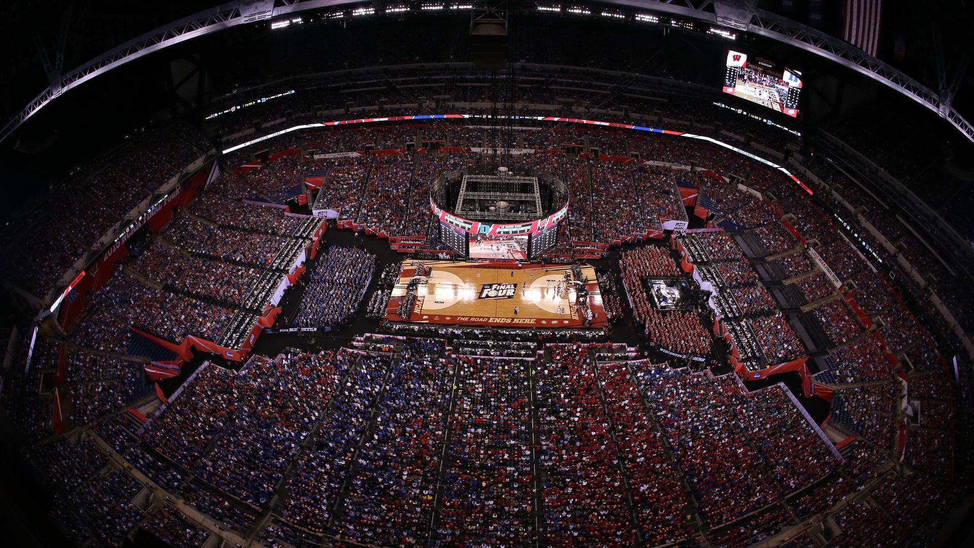 A crowded indoor basketball arena with fans in blue and red shirts surrounding a court displaying "Final Four" and "The Road Ends Here" signage during an NCAA event.