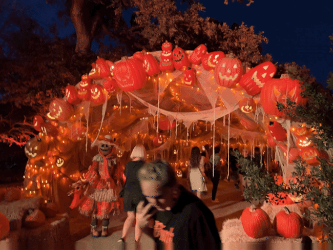 People walk through a tunnel decorated with pumpkins and orange lights.