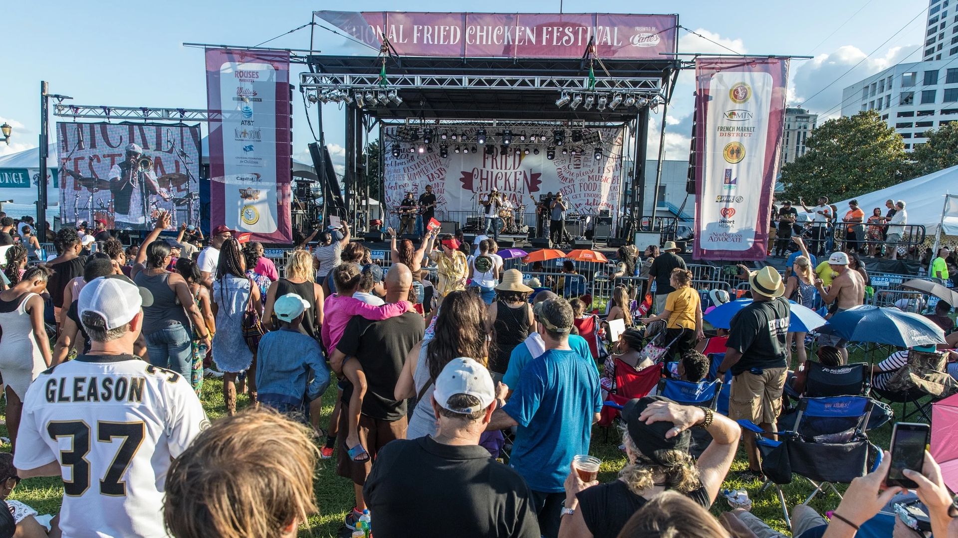 A crowd watches a performance in front of a stage with a banner that says Fried Chicken Festival.