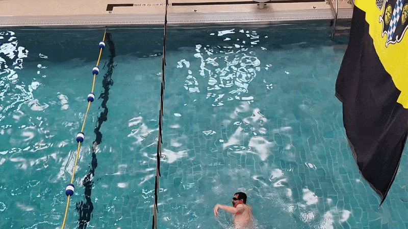 A man swimming in a pool underneath a yellow and black flag