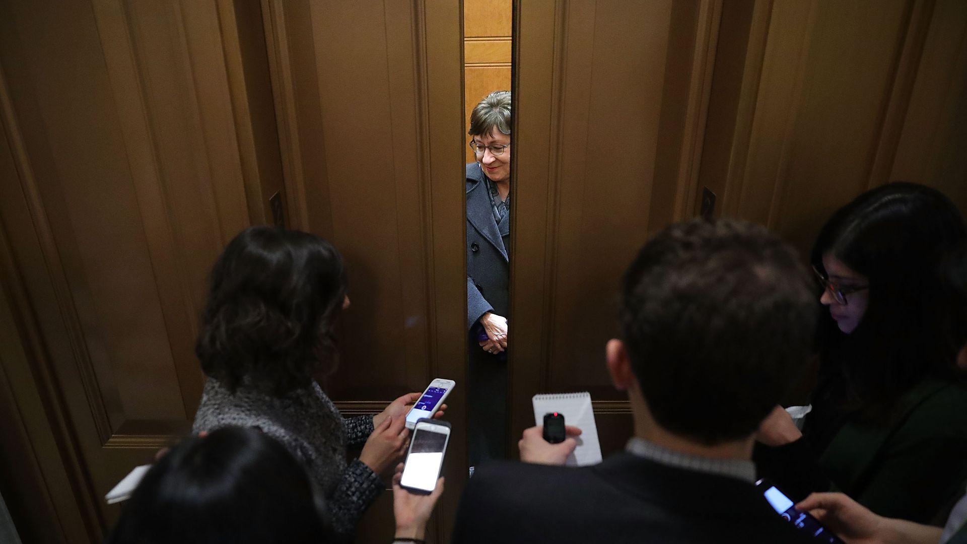 Susan Collins with elevator doors closing on her and reporters holding out recorders