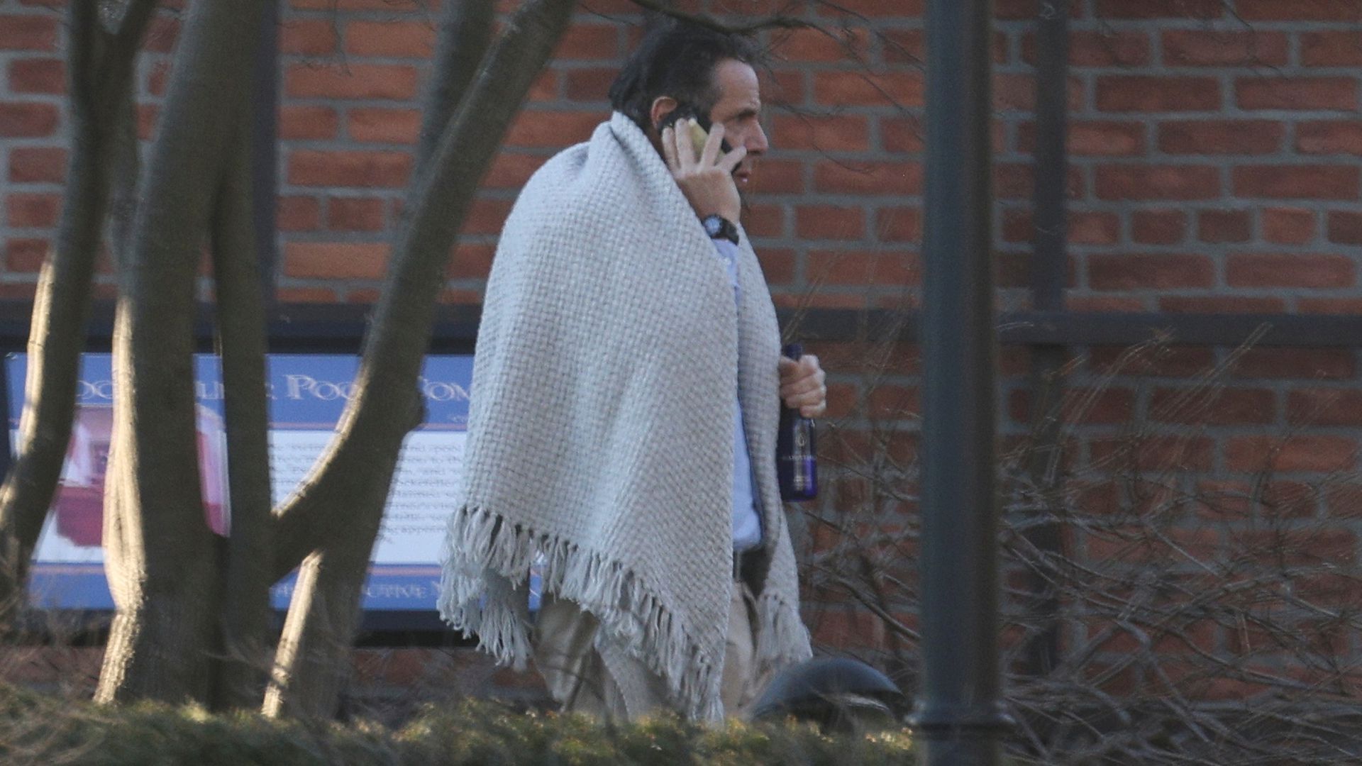 Picture of Andrew Cuomo with a blanket around his shoulders and holding a glass bottle