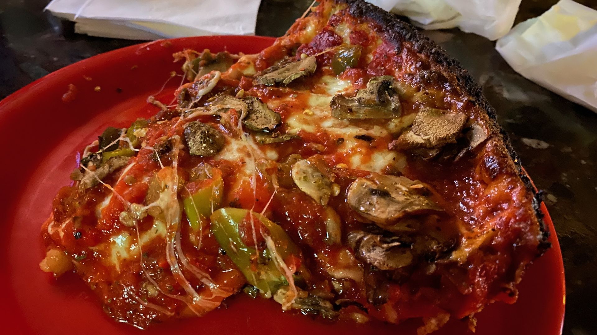 Piece of pizza with mushrooms, green peppers, red sauce and cheese on a red plate.