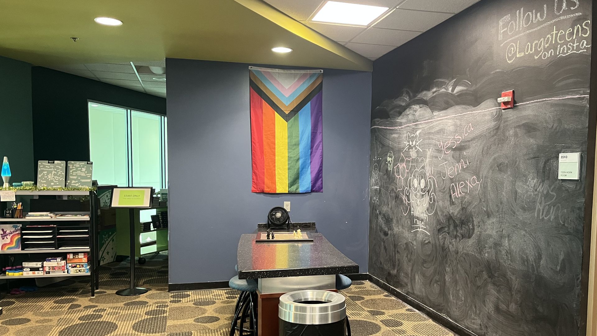 A Progress Pride flag hangs on a blue wall.