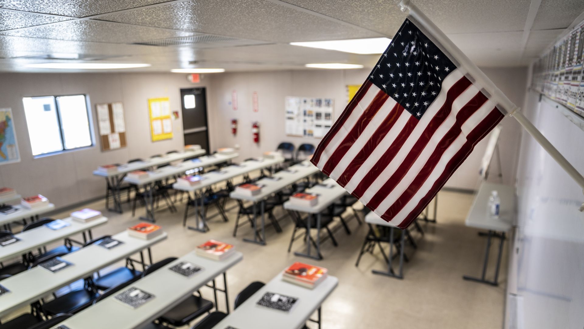 Text books and notebooks line tables inside a classroom at a Influx Care Facility (ICF) for unaccompanied children
